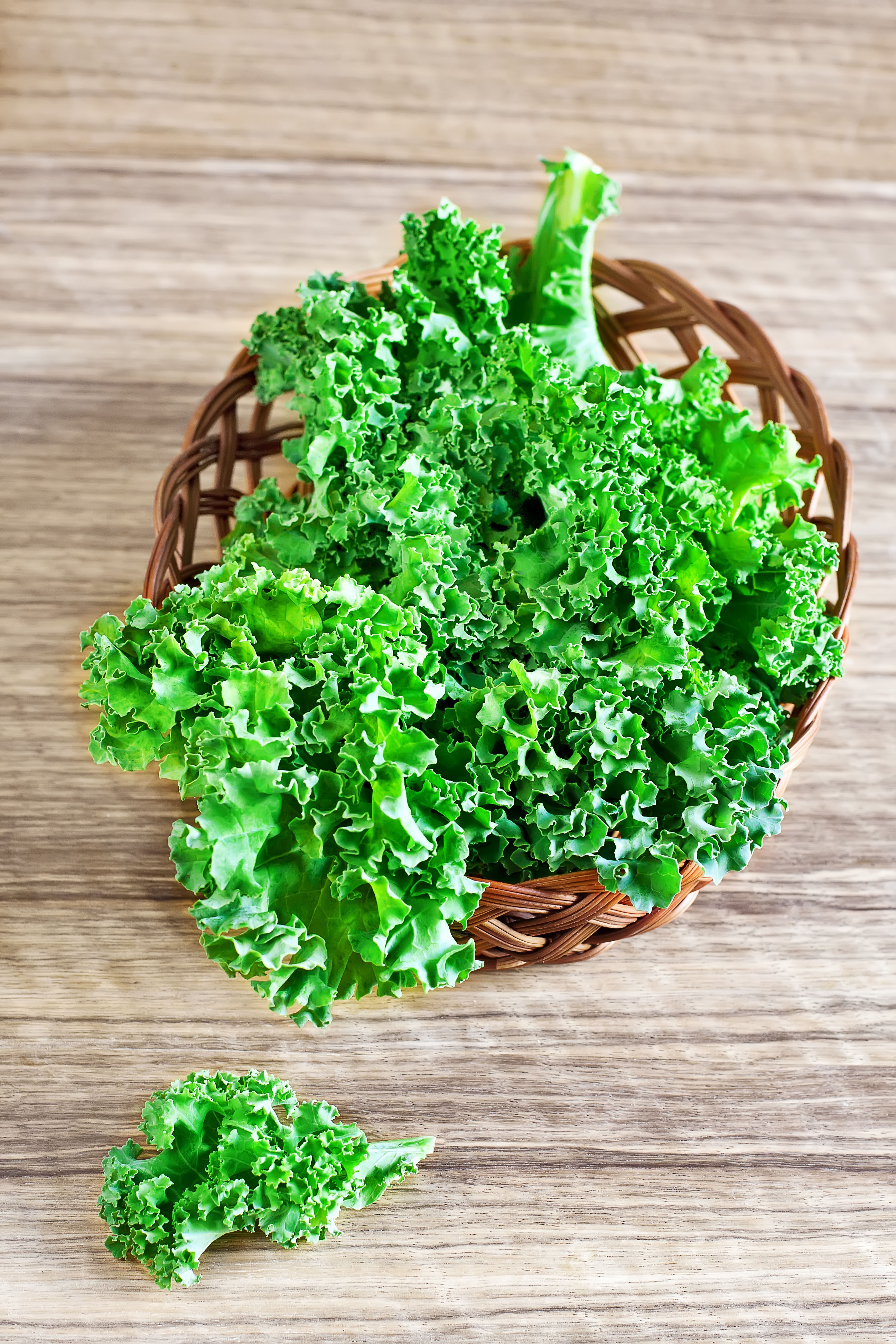 A basket of fresh green kale leaves on a wooden table 