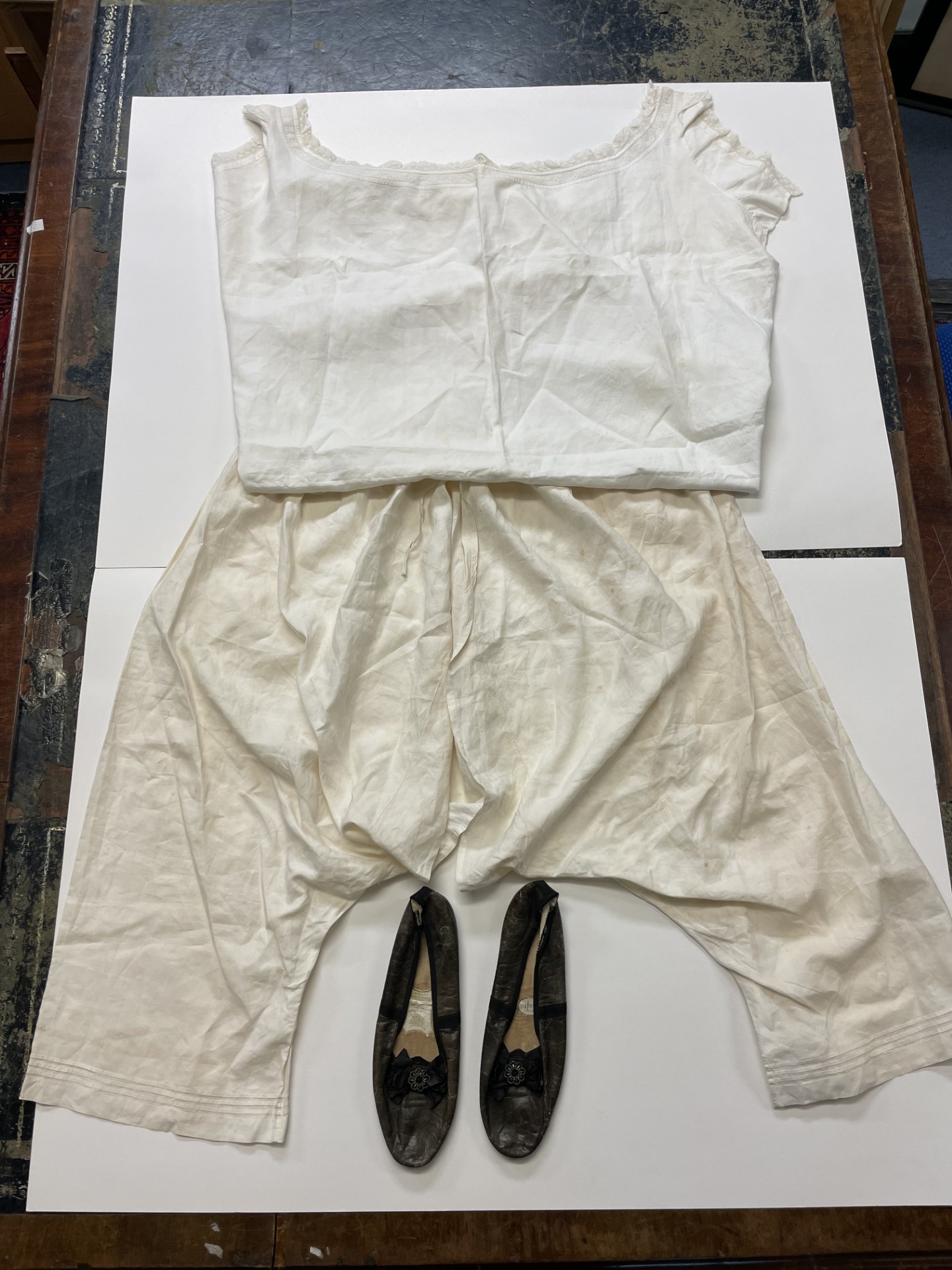 The white chemise and bloomers and dark leather shoes laid out on a table