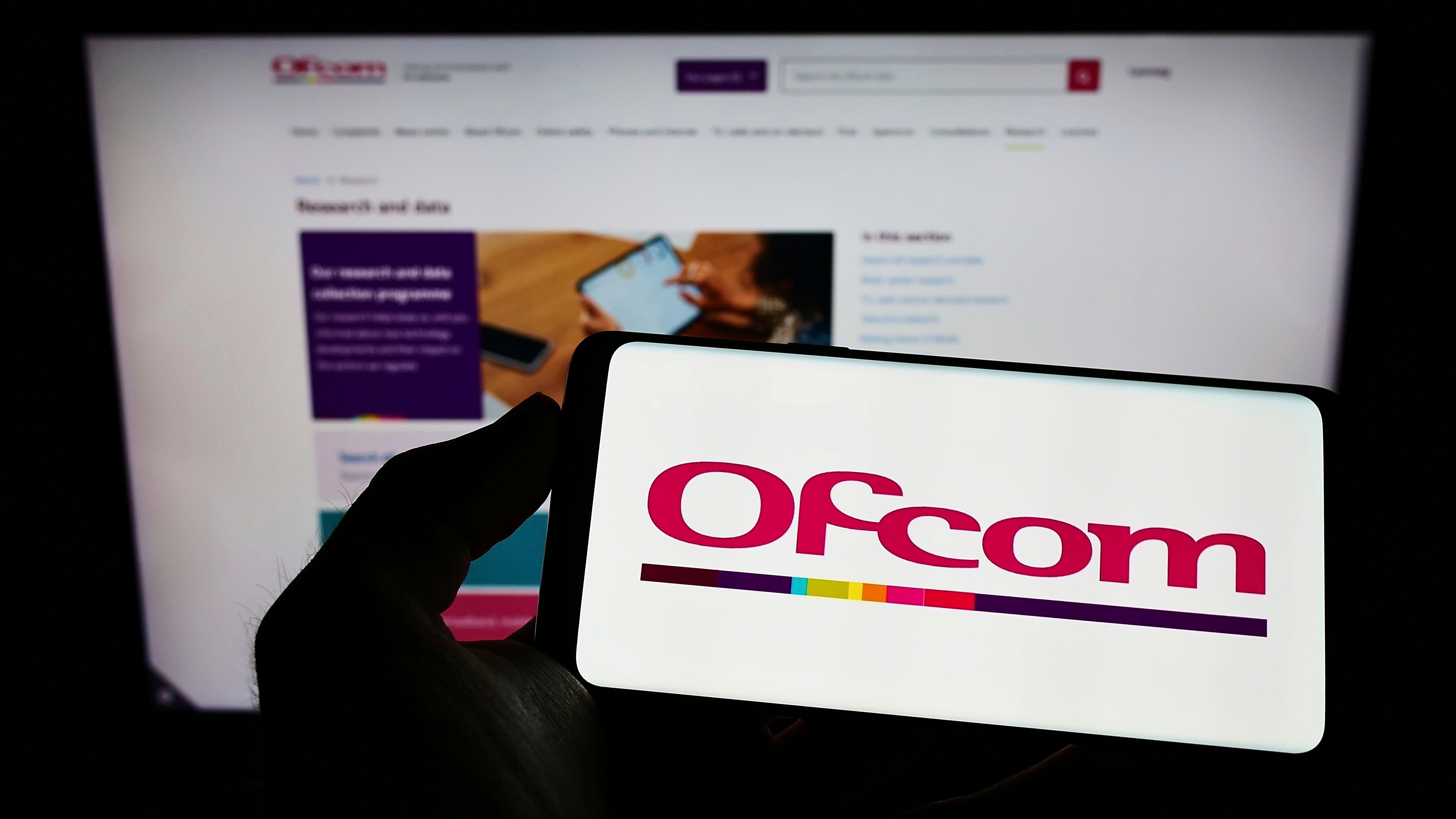 A person holding a mobile phone with a logo of Ofcom on the screen