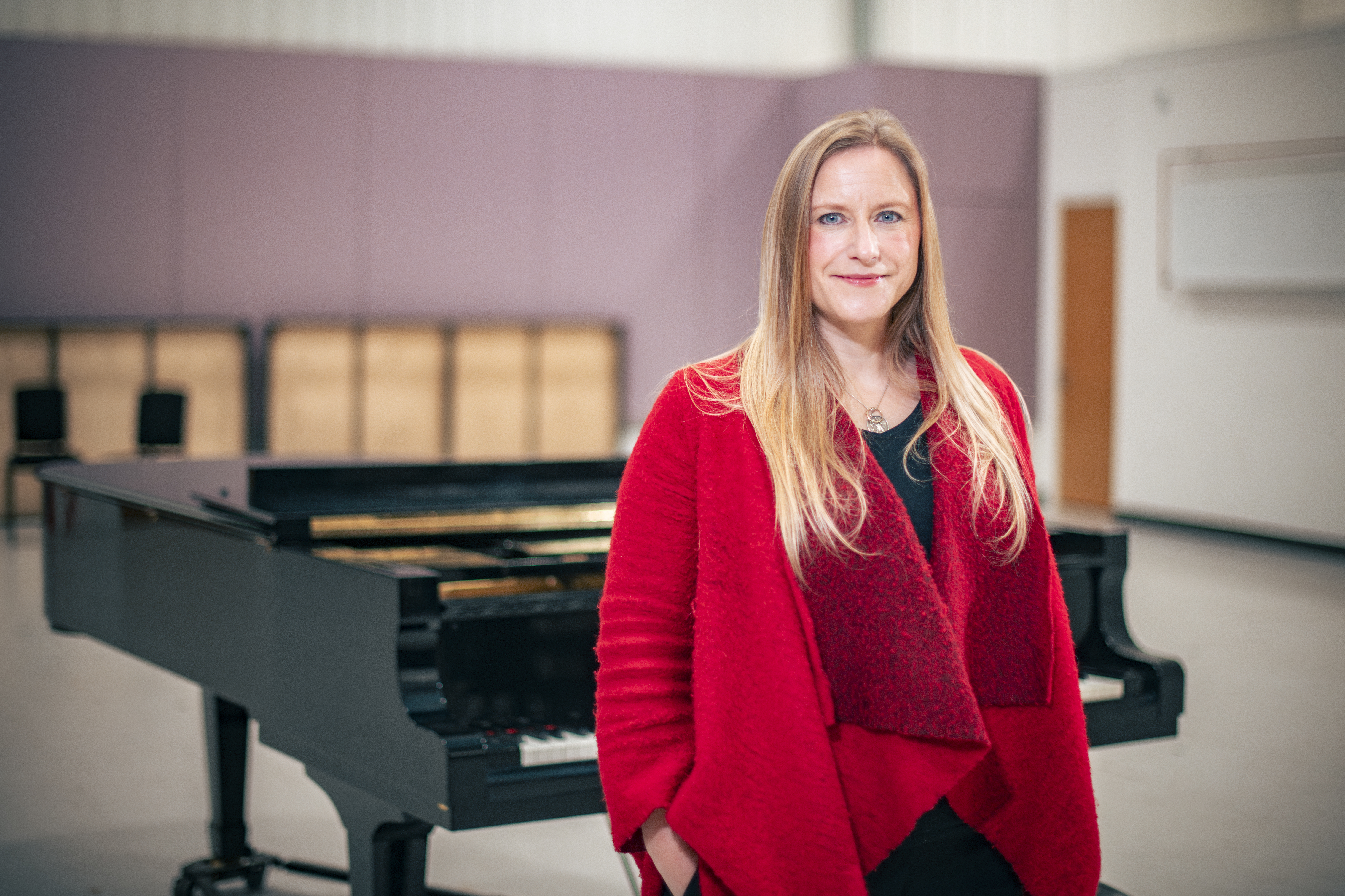 Playwright Frances Poet in a red top standing in front of a grand piano