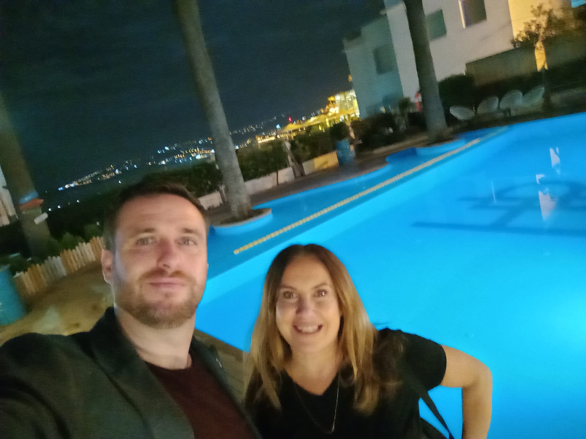 A man and woman smiling in front of a swimming pool