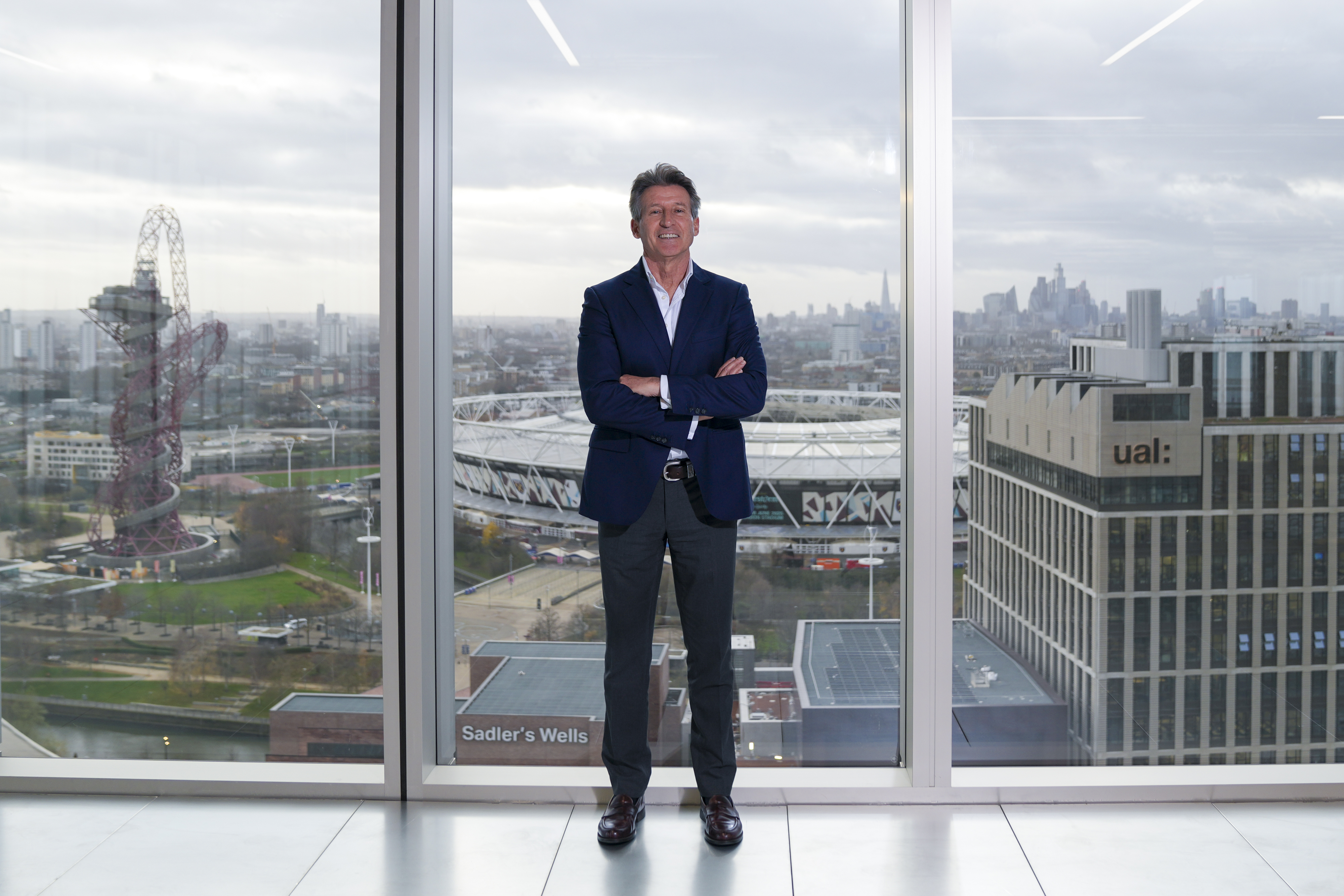 Sebastian Coe pictured in front of floor to ceiling glass windows,with the Olympic Park in London in the backdrop