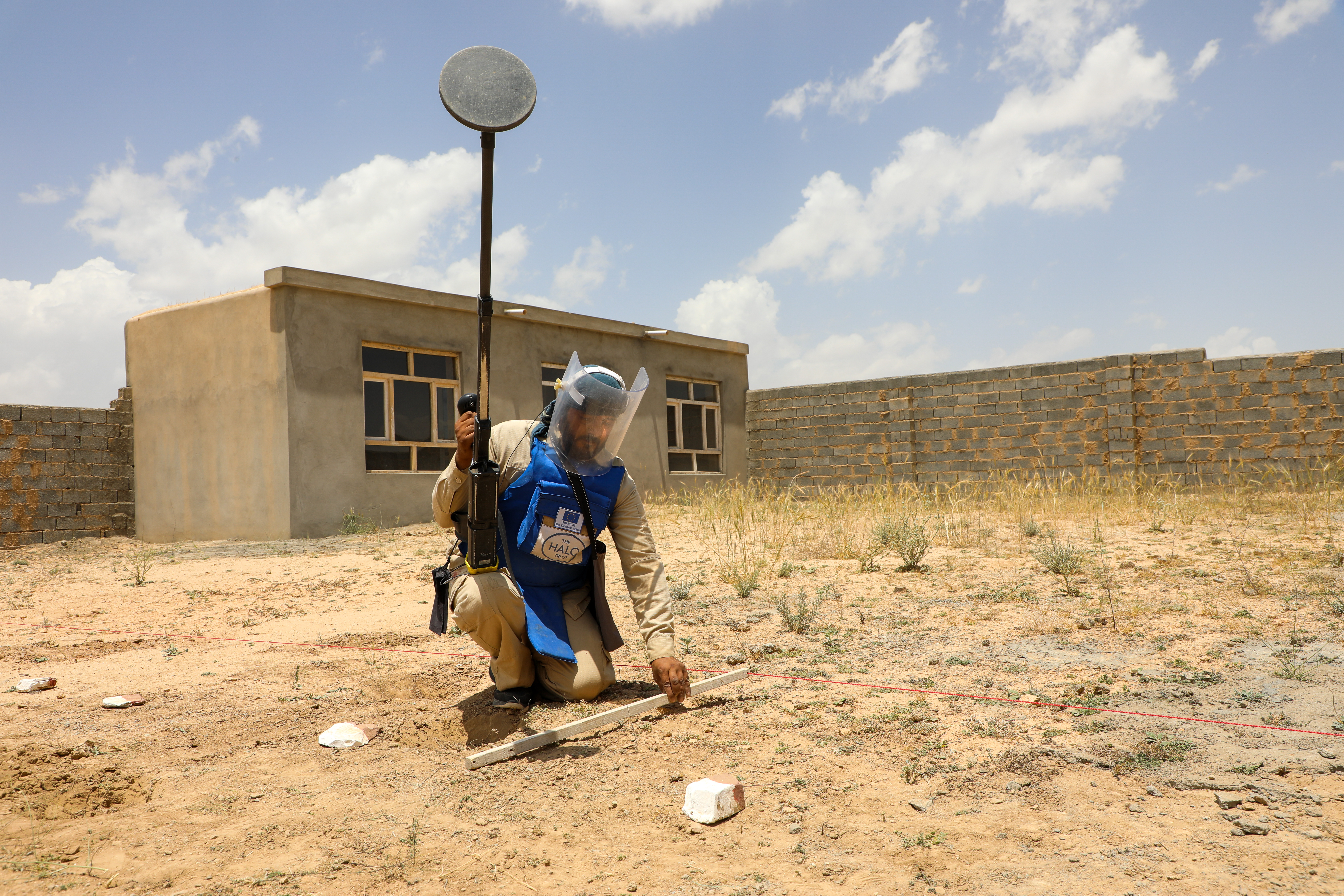 Man with metal detector and wearing protective equipment checks and area of scrubland