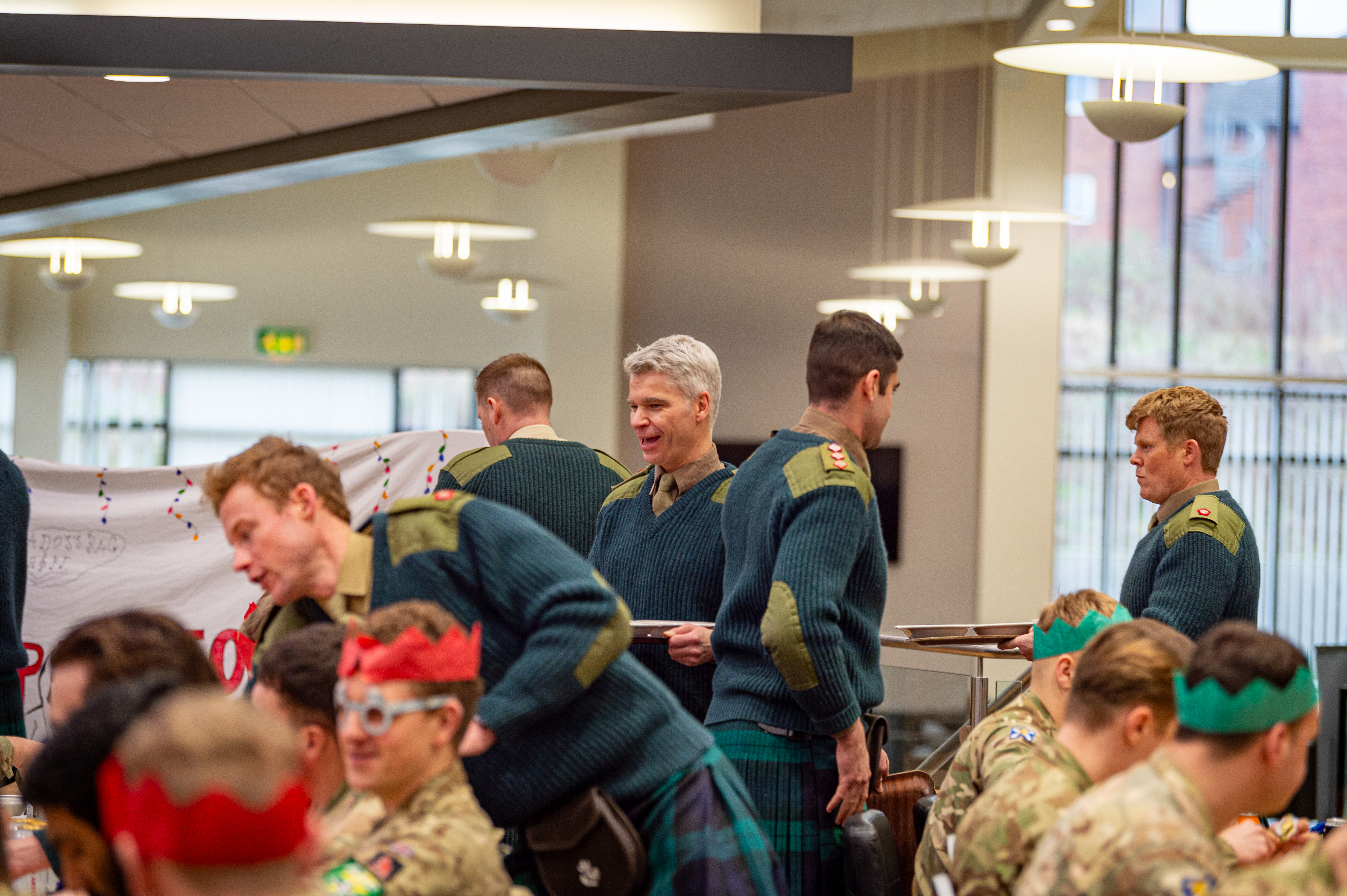 Officers and soldiers in mess hall, some party Christmas cracker hats