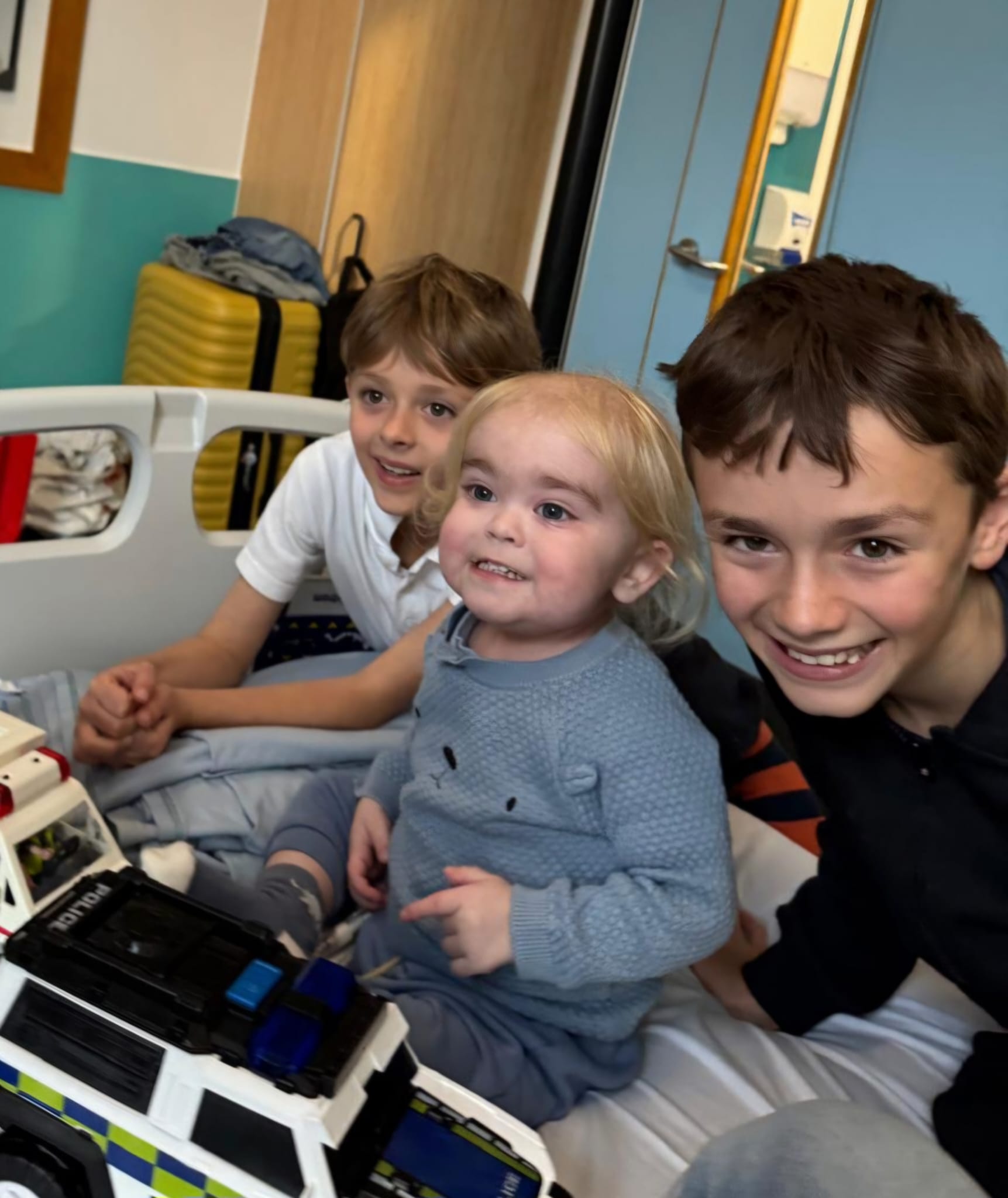 Bobby (left), Alfie (centre) and Teddie (right) smiling as they sit on a hospital bed at Great Ormond Street Hospital 