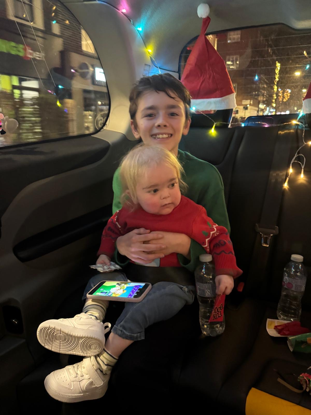 Teddie smiling at the camera with Alfie sat on his knee in the black cab