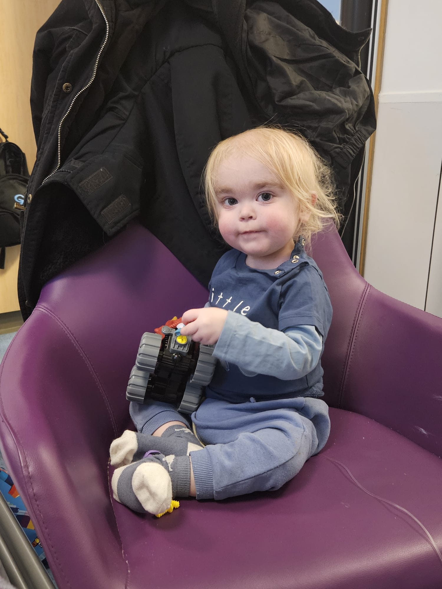 Alfie playing with a toy car while sat on a chair at the hospital