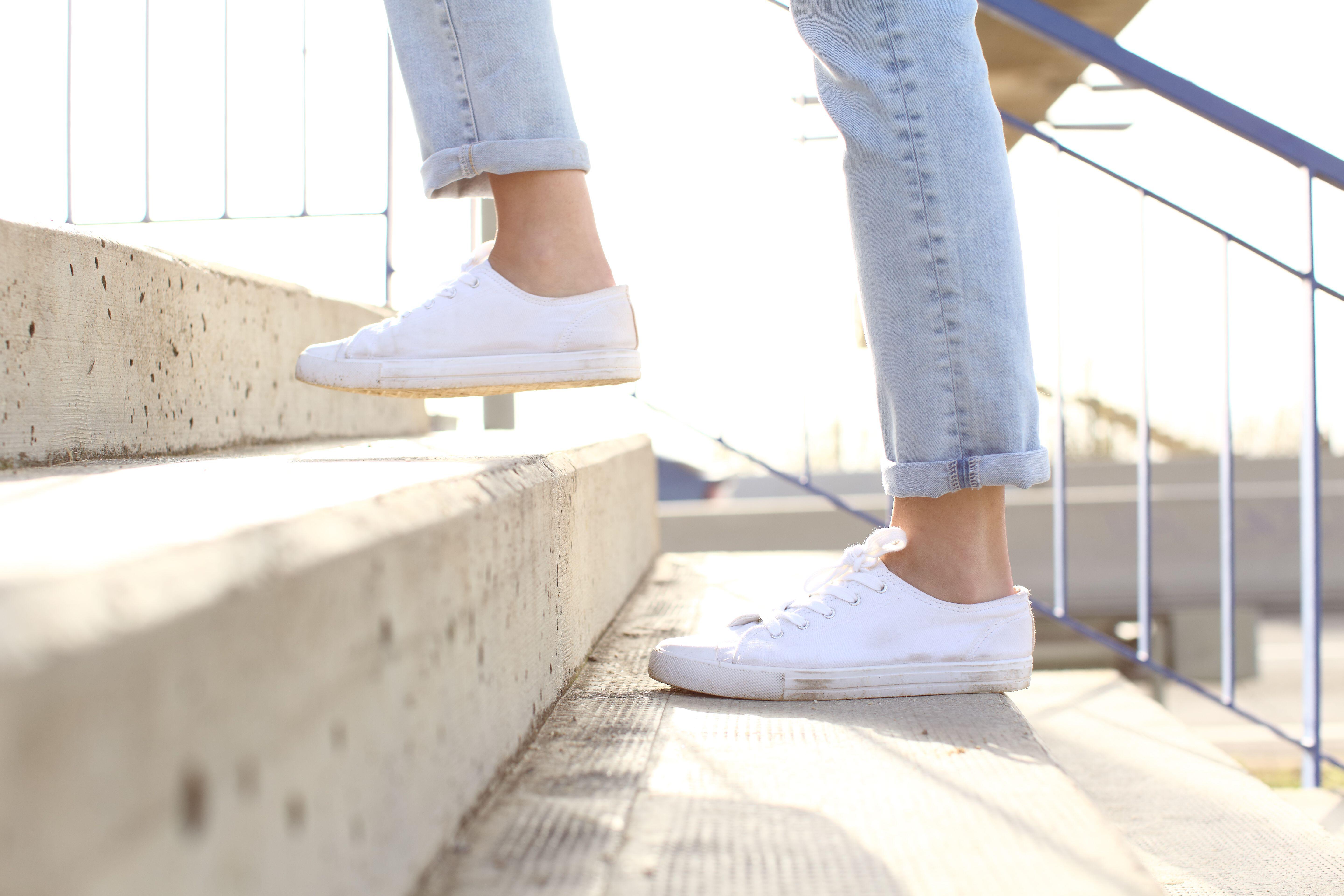 Close up picture of a woman who is wearings white trainers and grey jeans walking up some stairs 