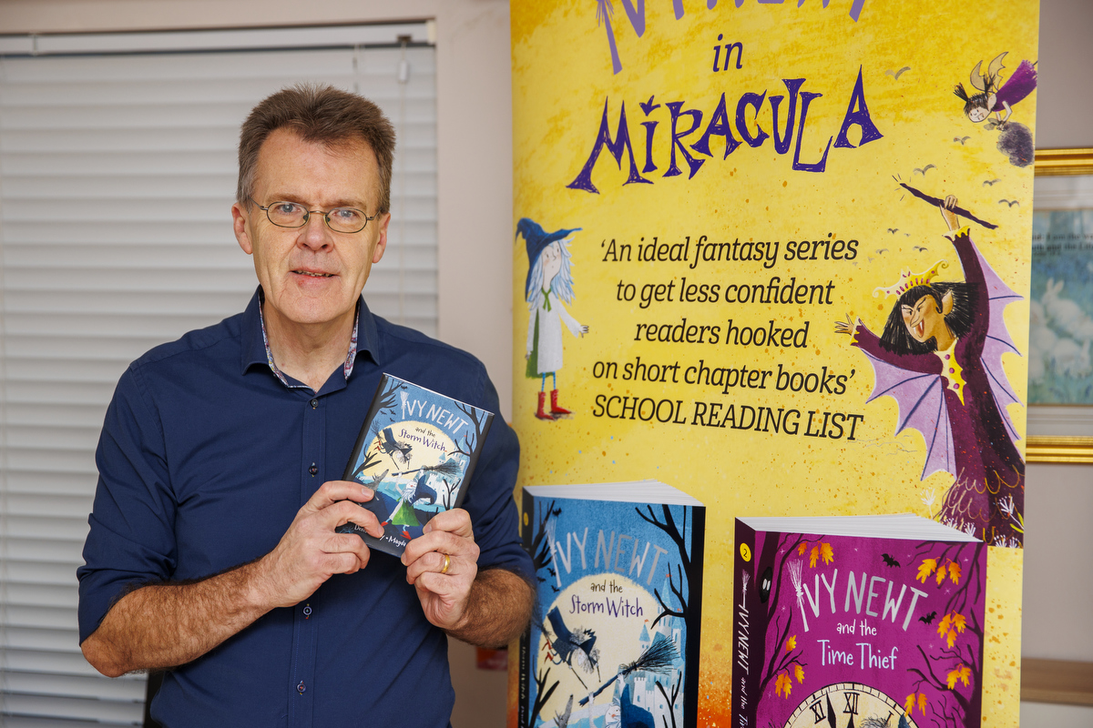 Derek Keilty holding an Ivy Newt book next to a promotional poster