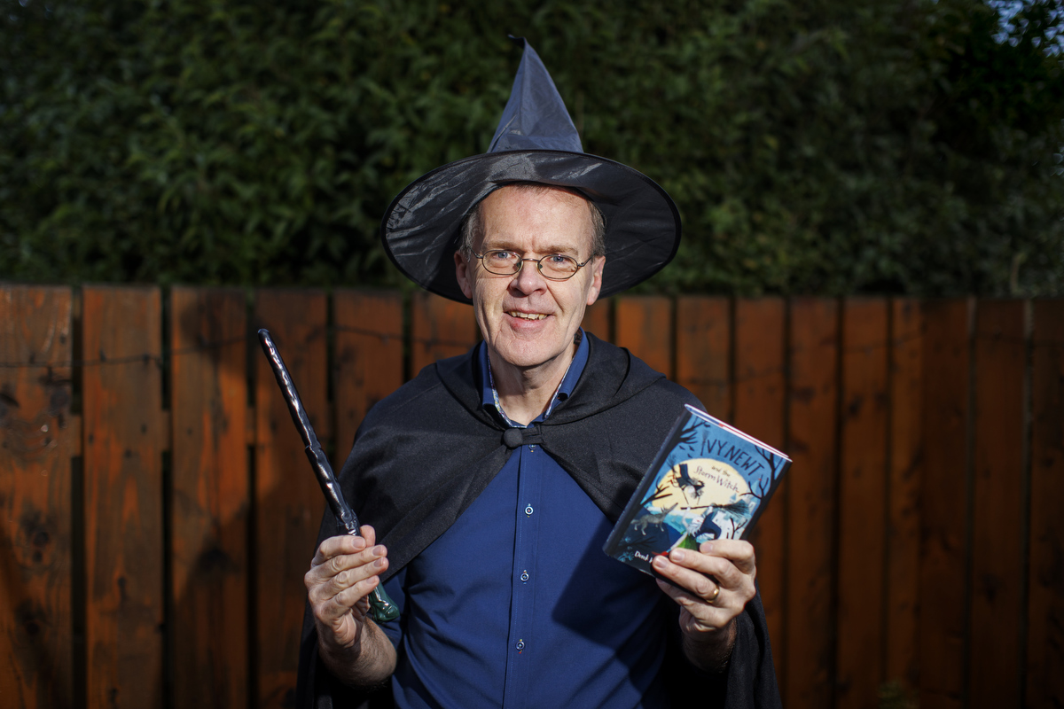 Derek Keilty in a wizard's hat while holding a magic wand in one hand and an Ivy Newt book in the other