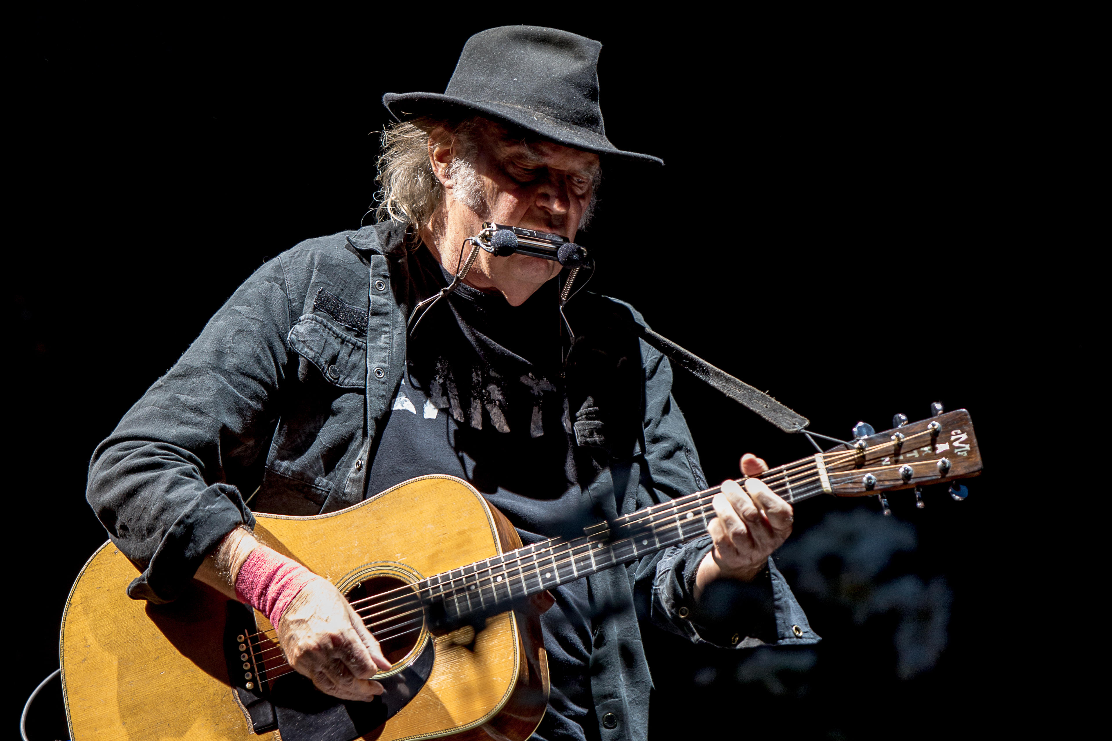 Neil Young perform performing with guitar and mouth organ