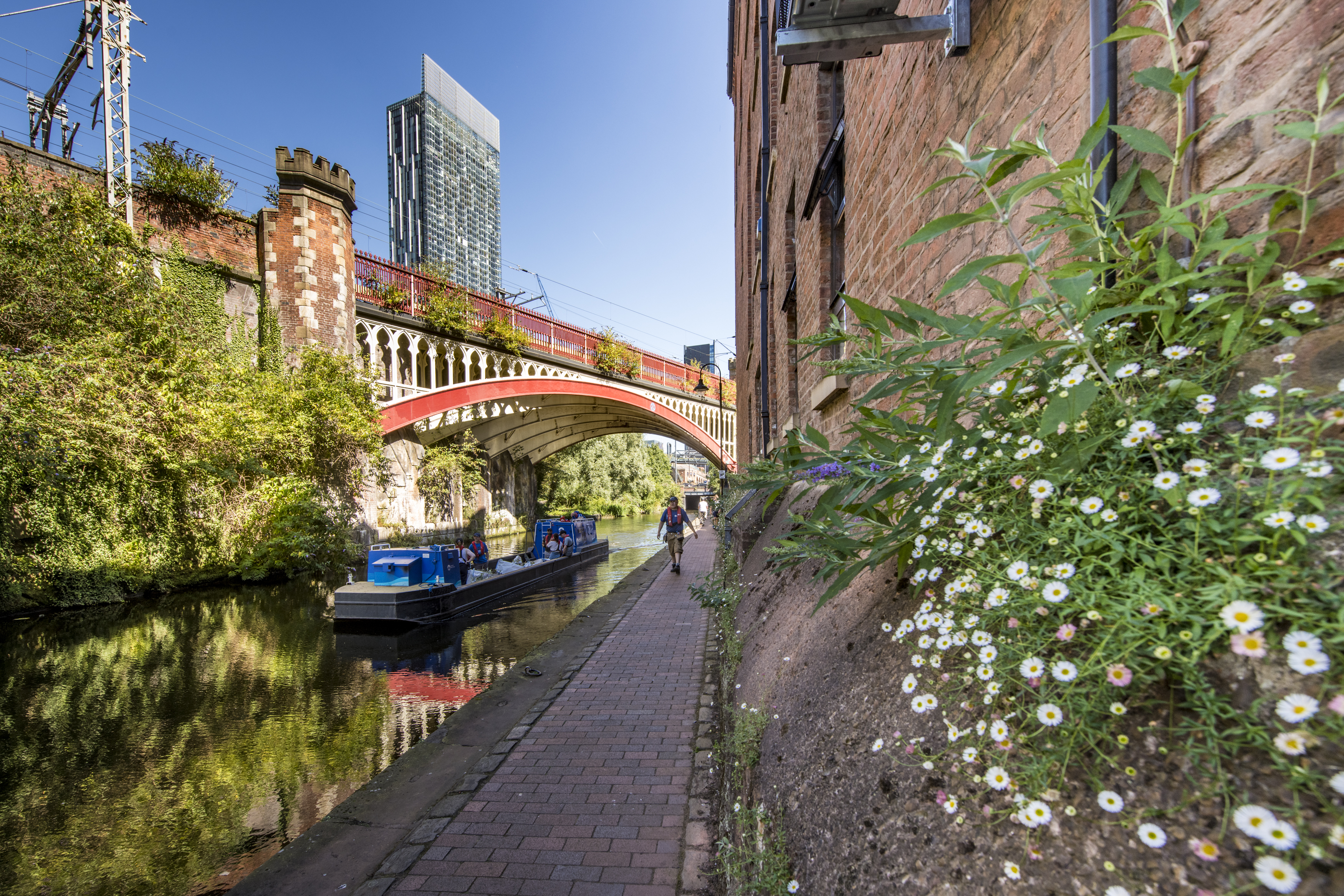 Boat on a canal with flowers close to the towpath and high rise buildings in Manchester