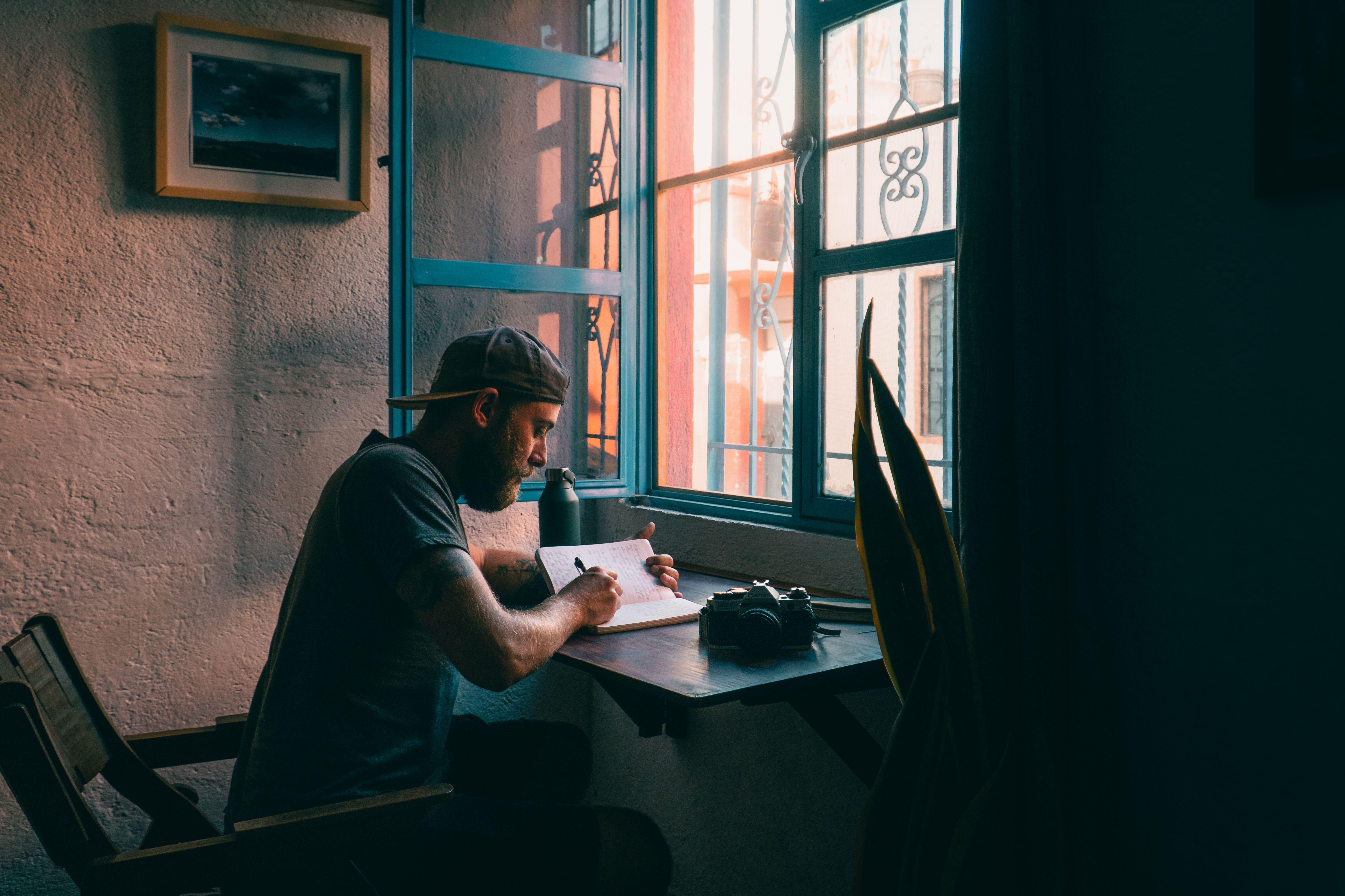 Male sits at wooden desk in a small dimly lit apartment 