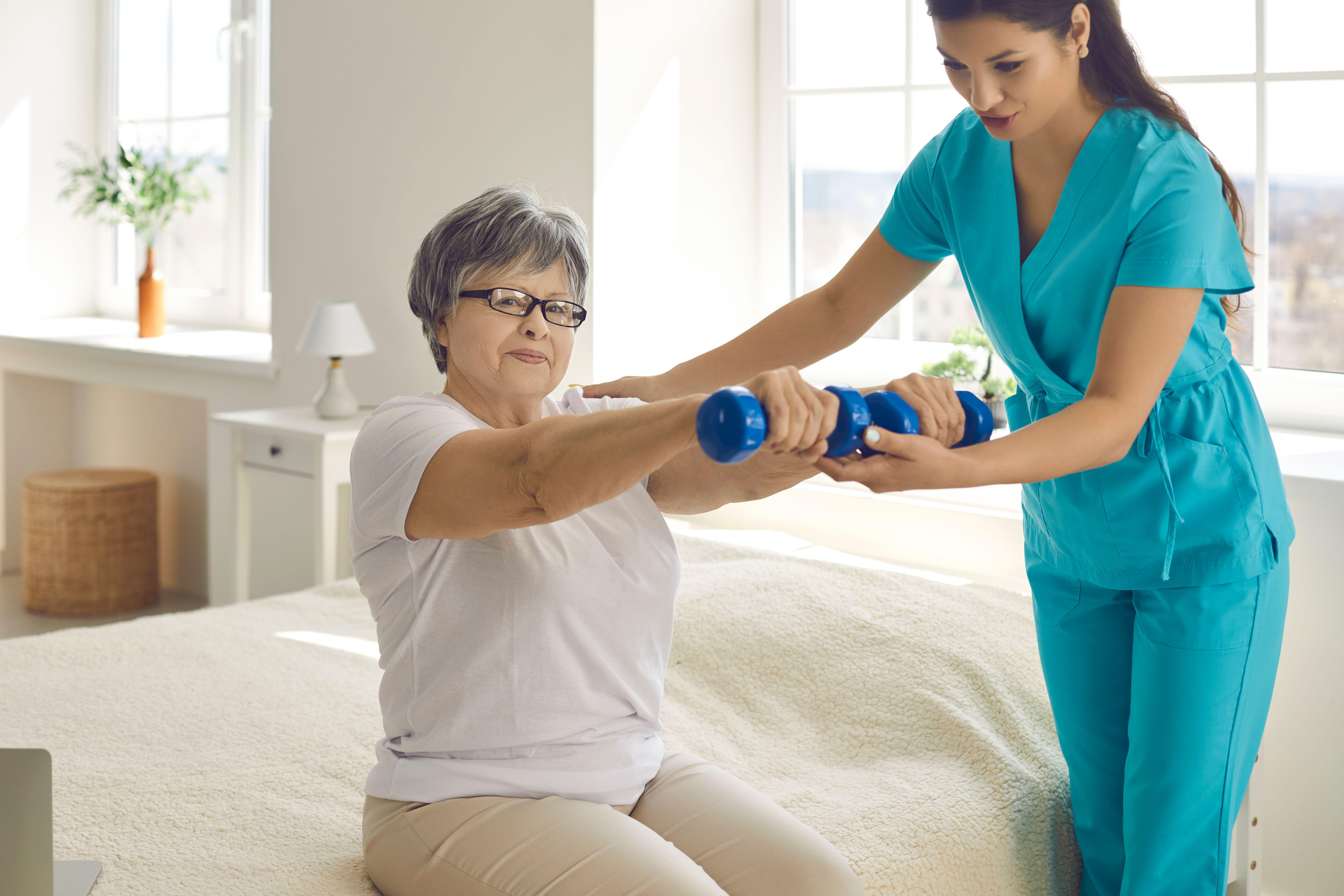 Physiotherapist helping senior woman lifting hand held weights for rehabilitation exercises