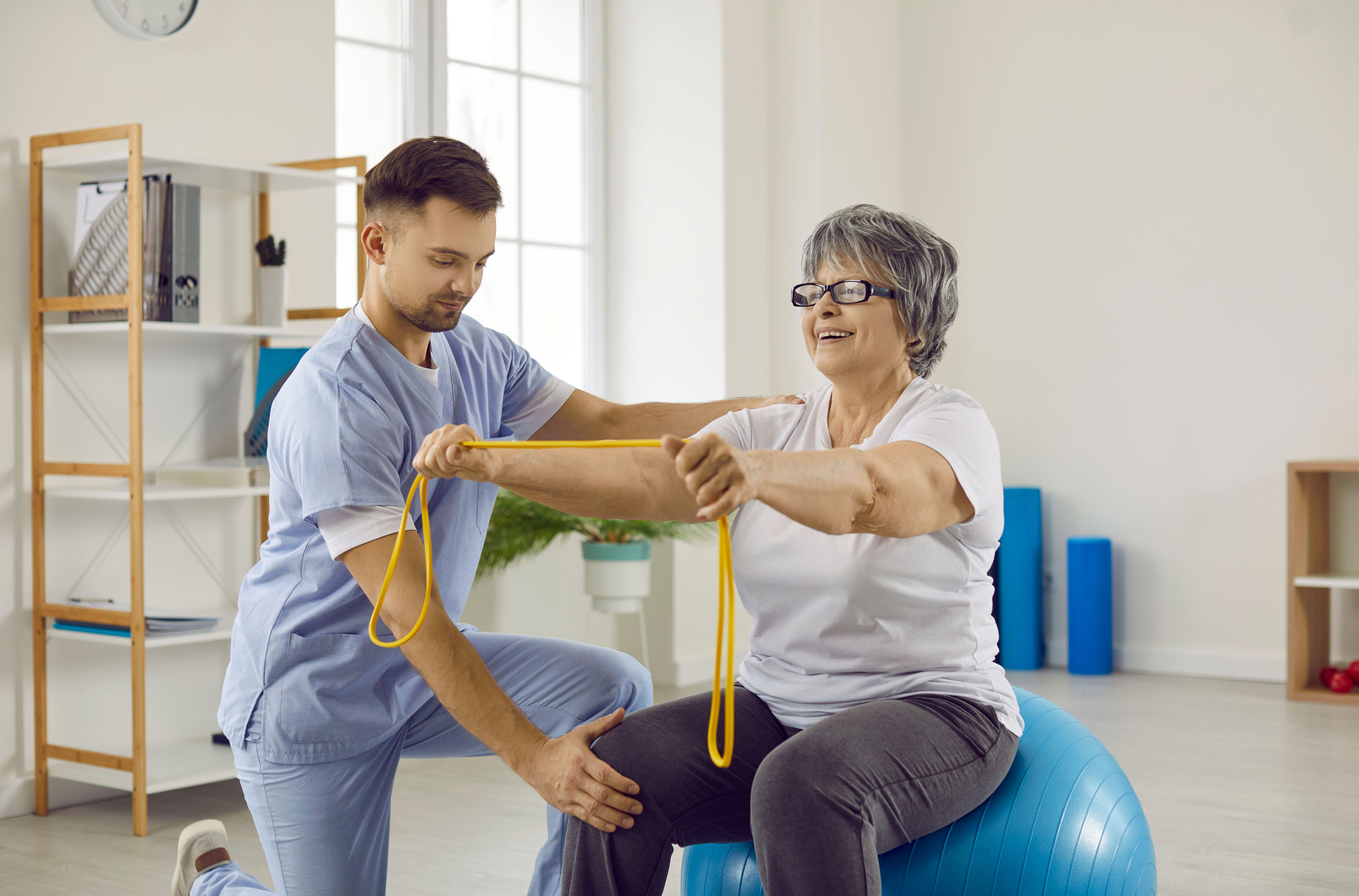 Physiotherapist helping senior woman with osteoporosis do exercises on an exercise ball 