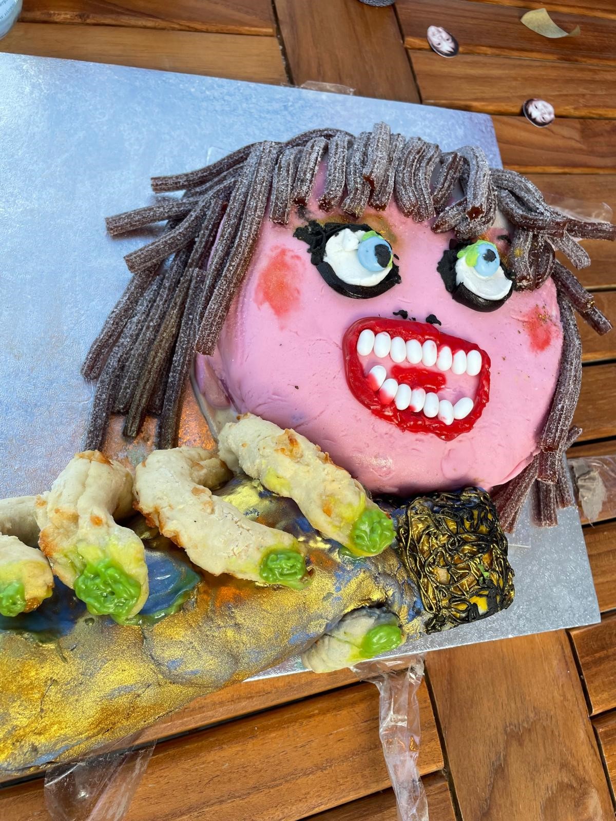 Image of a caricature-style cake of Taylor Swift with fizzy cola straw sweets for hair, large fingers holding a microphone and pink icing for skin