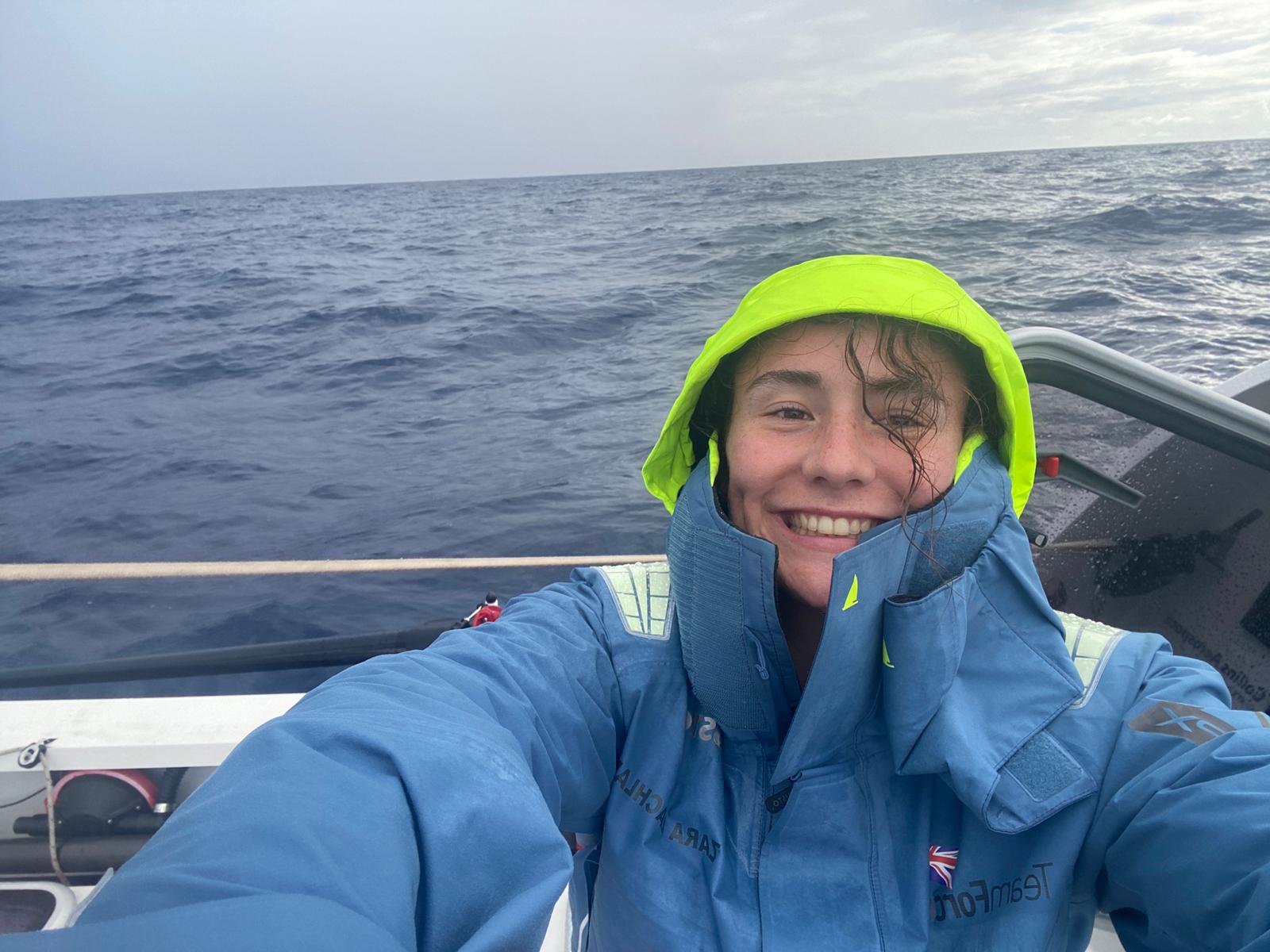 Woman wearing blue rain coat while sat on a rowing boat at sea