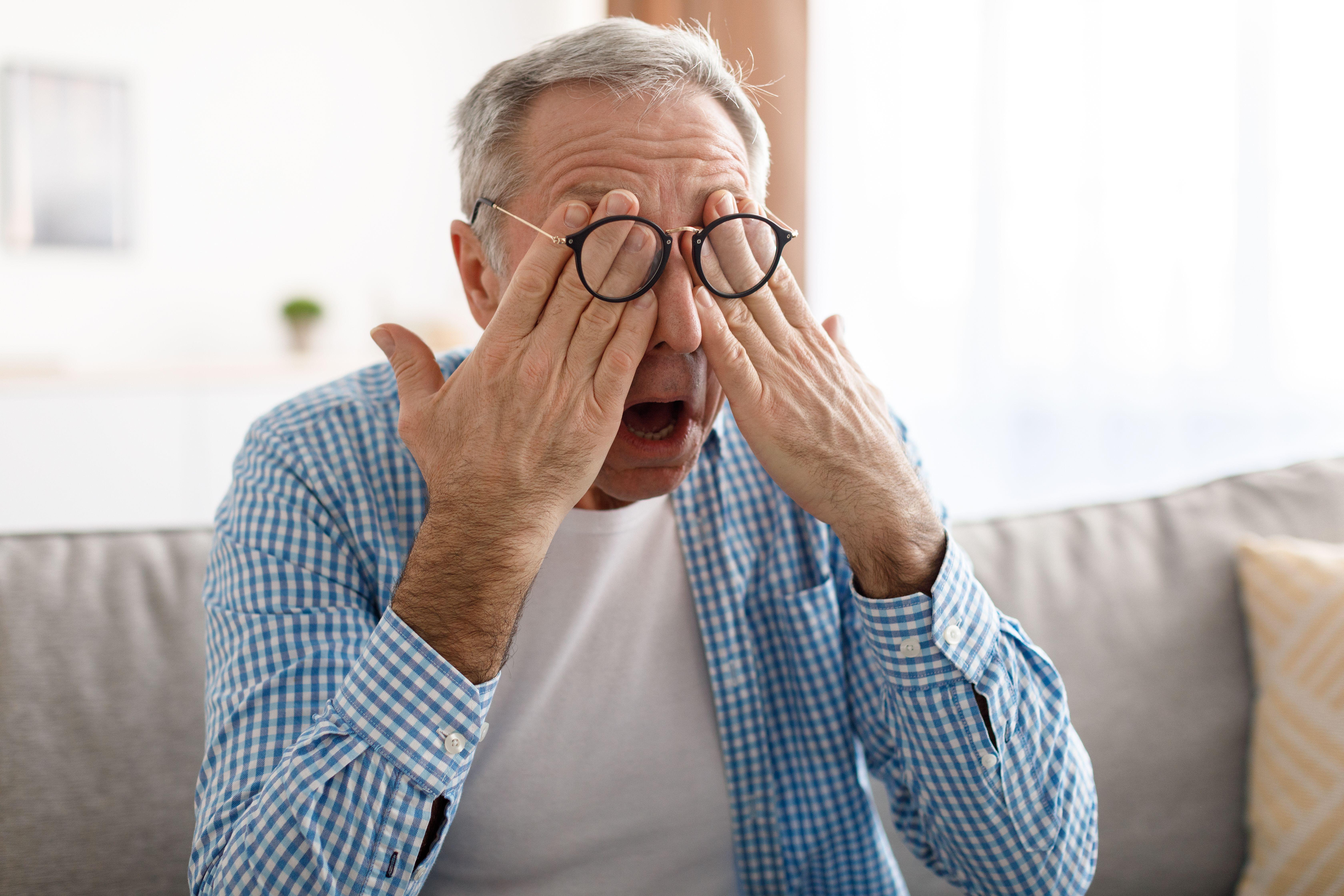 Senior man rubbing his tired eyes while wearing glasses 