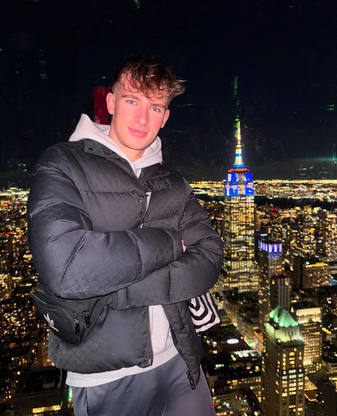 Man in black puffer jacket poses in front of backdrop of a city skyline