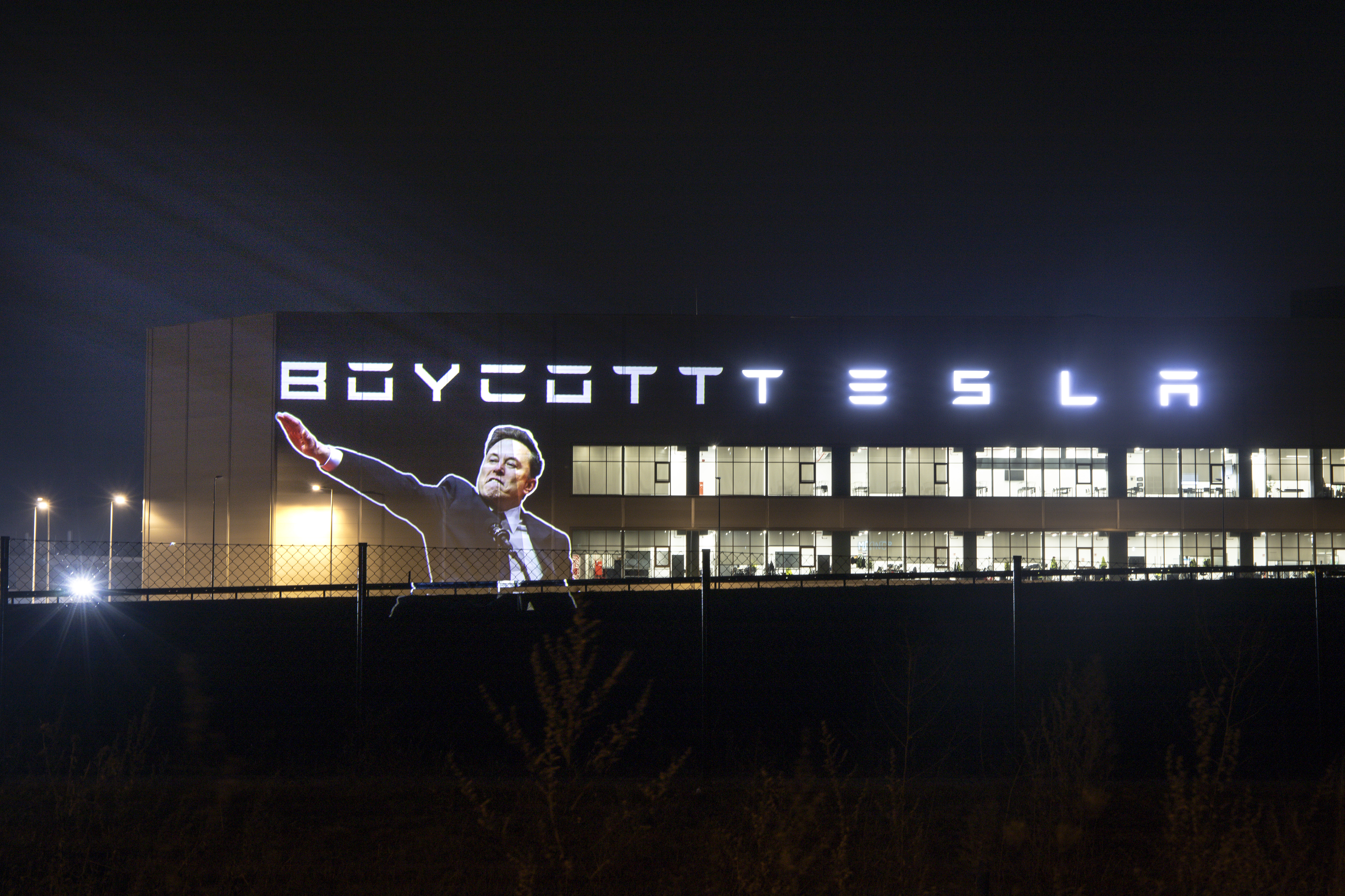 Image of Elon Musk making a hand gesture widely interpreted as a Nazi salute projected onto the side of a Tesla building with the words 'Boycott Tesla'