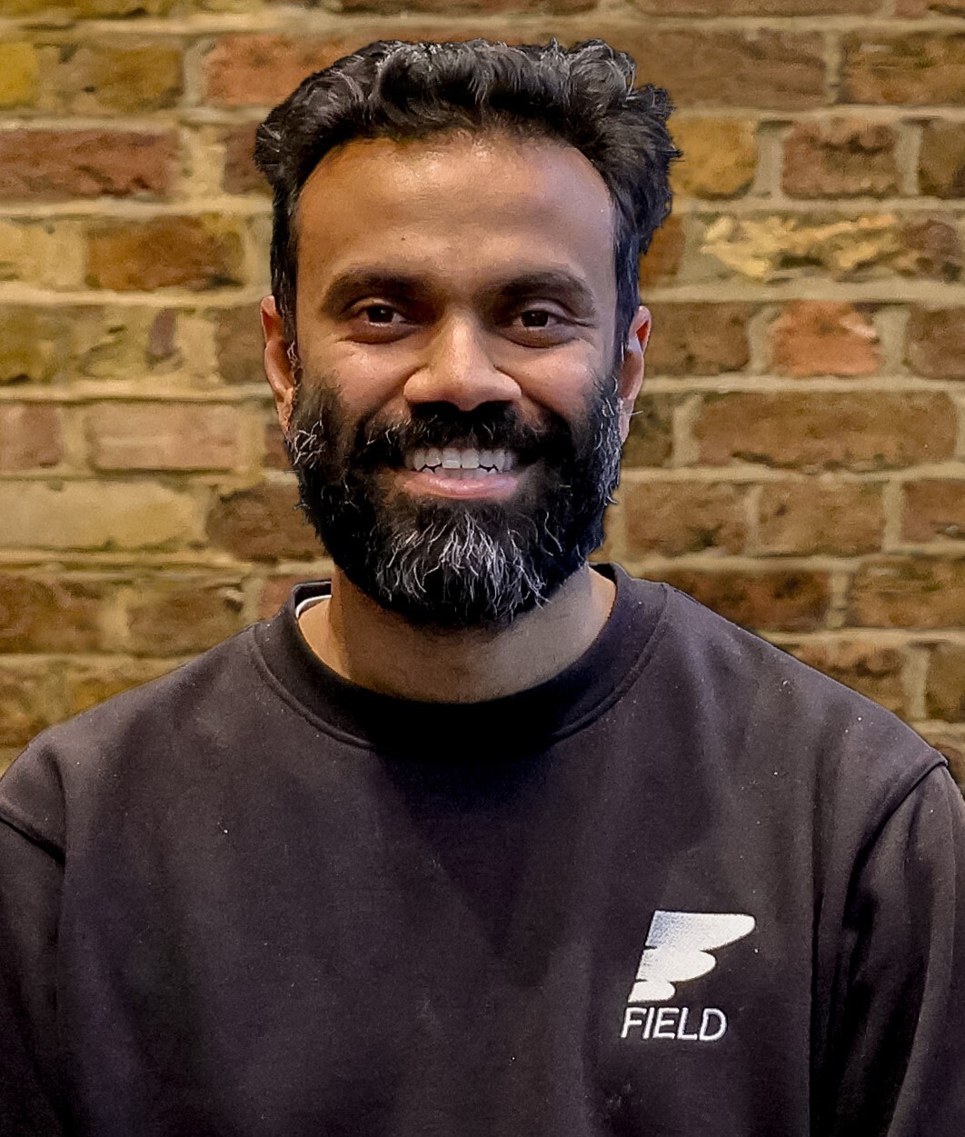 Handout photo of Amit Gudka smiling, wearing black jumper featuring the Field logo