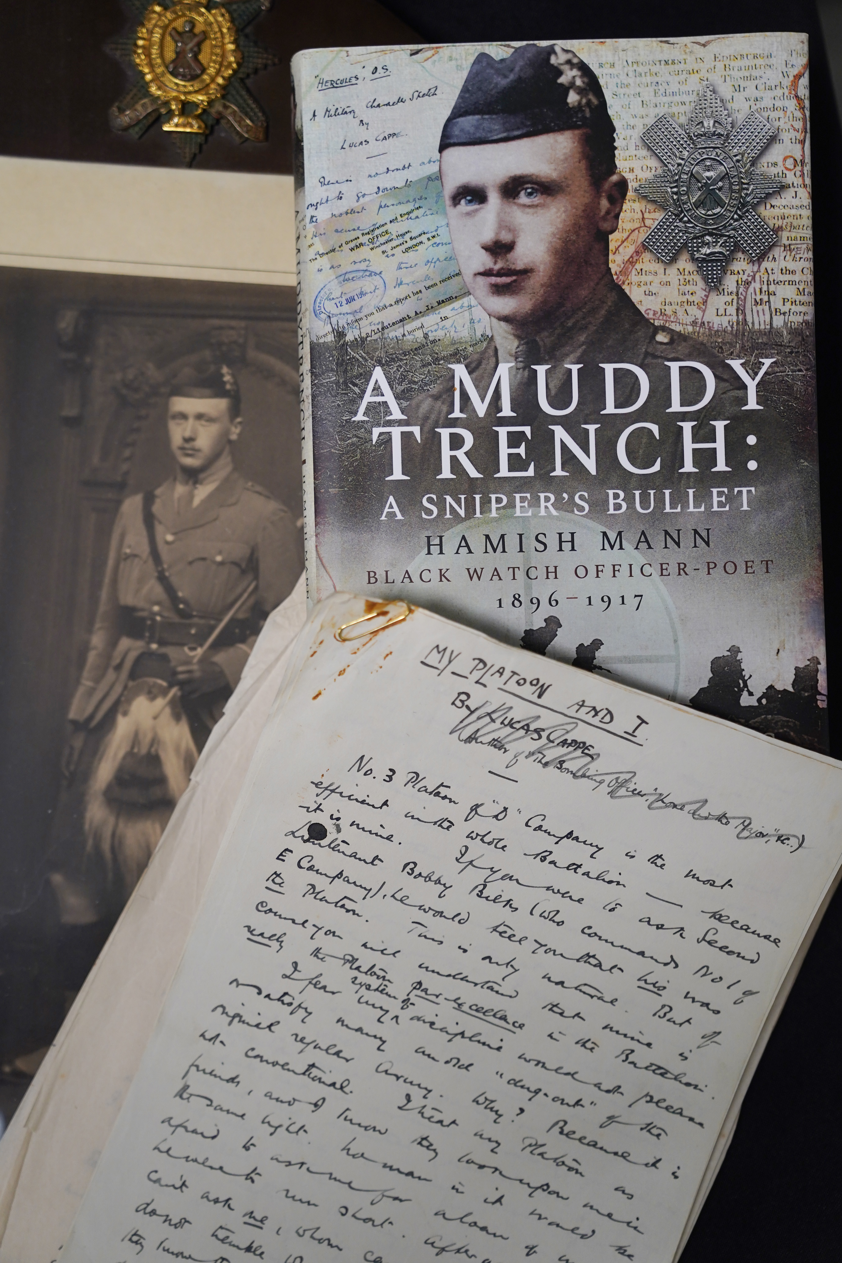 A4 paper covered in hand-written prose, on top of a black and white photograph of a soldier in a kilt, and a hard-backed book entitled A Muddy Trench