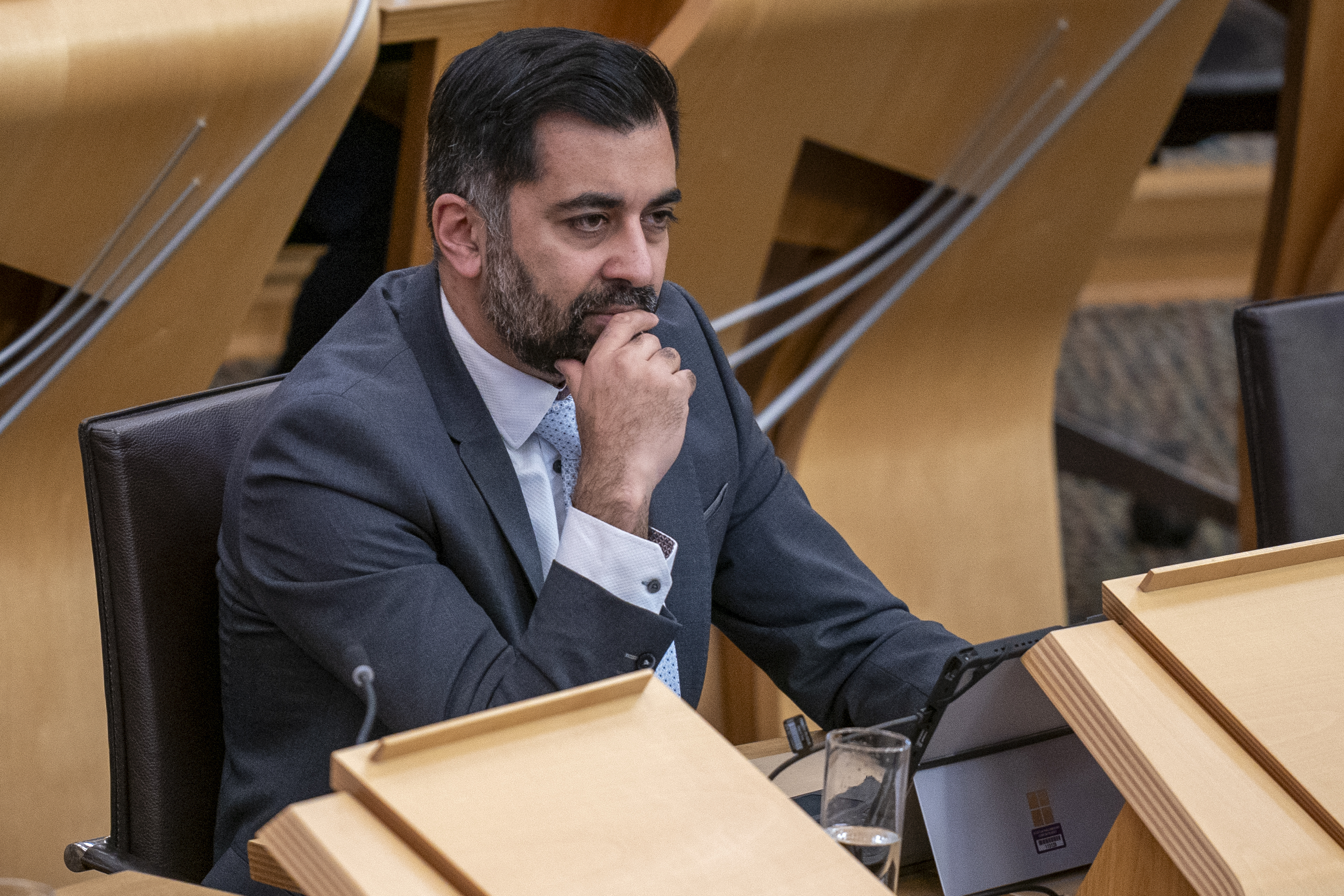 Humza Yousaf sitting at a desk in the Holyrood chamber, with one hand resting on his chin