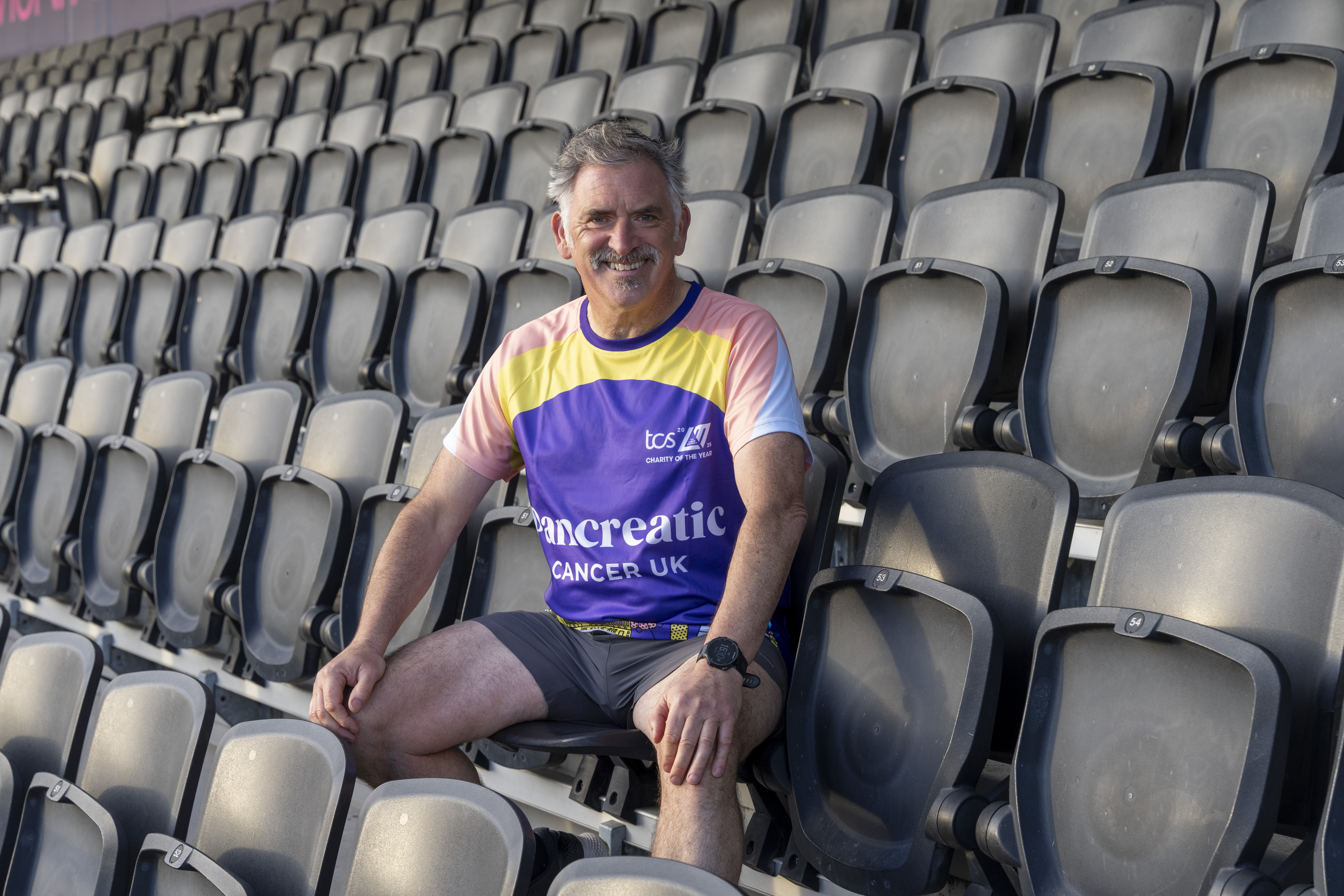 Tony Audenshaw smiling while wearing running kit while sat in the stands at the London Marathon Community Track in Stratford, east London