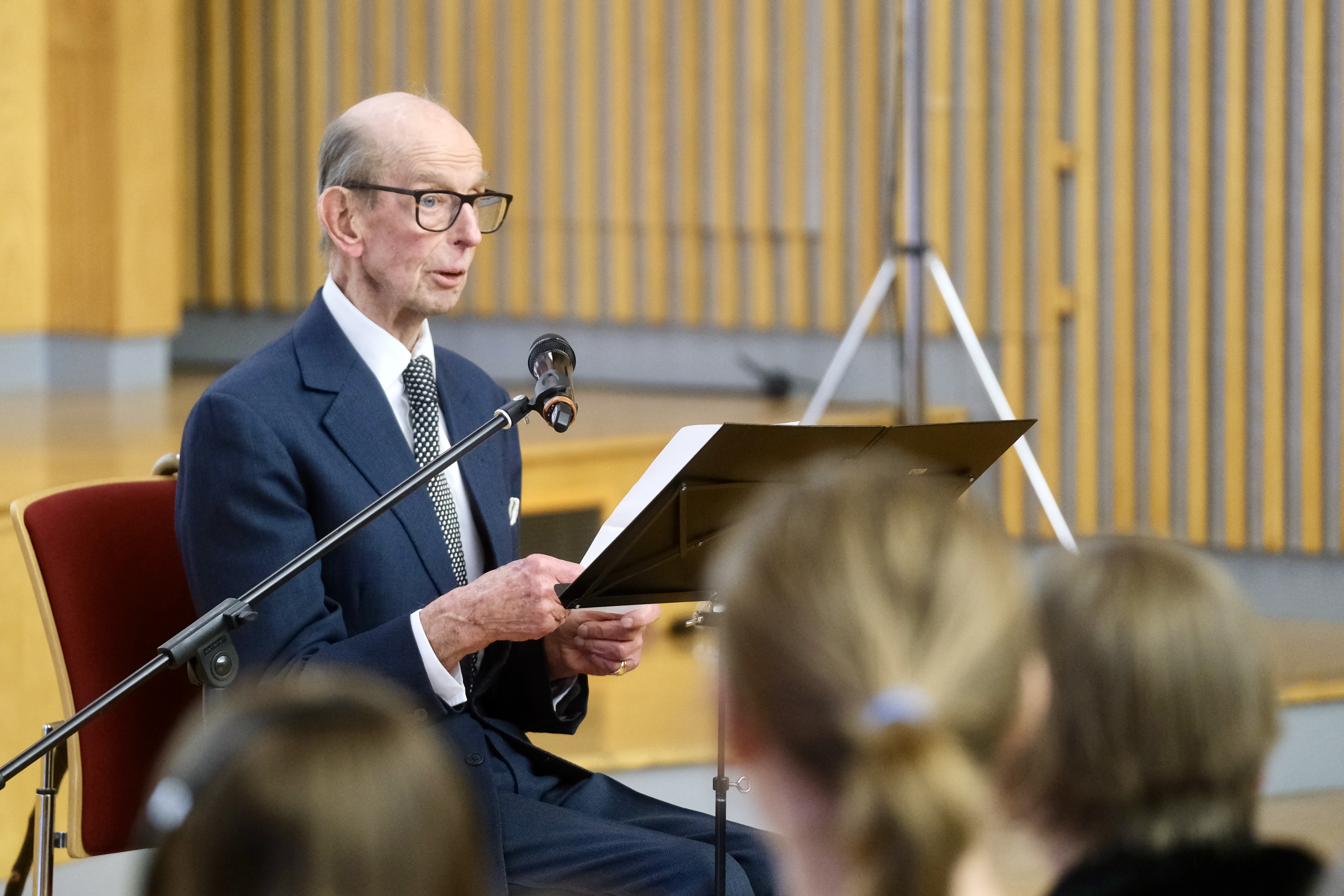 The Duke of Kent sits at a lectern with a microphone in front of him and delivers his speech 