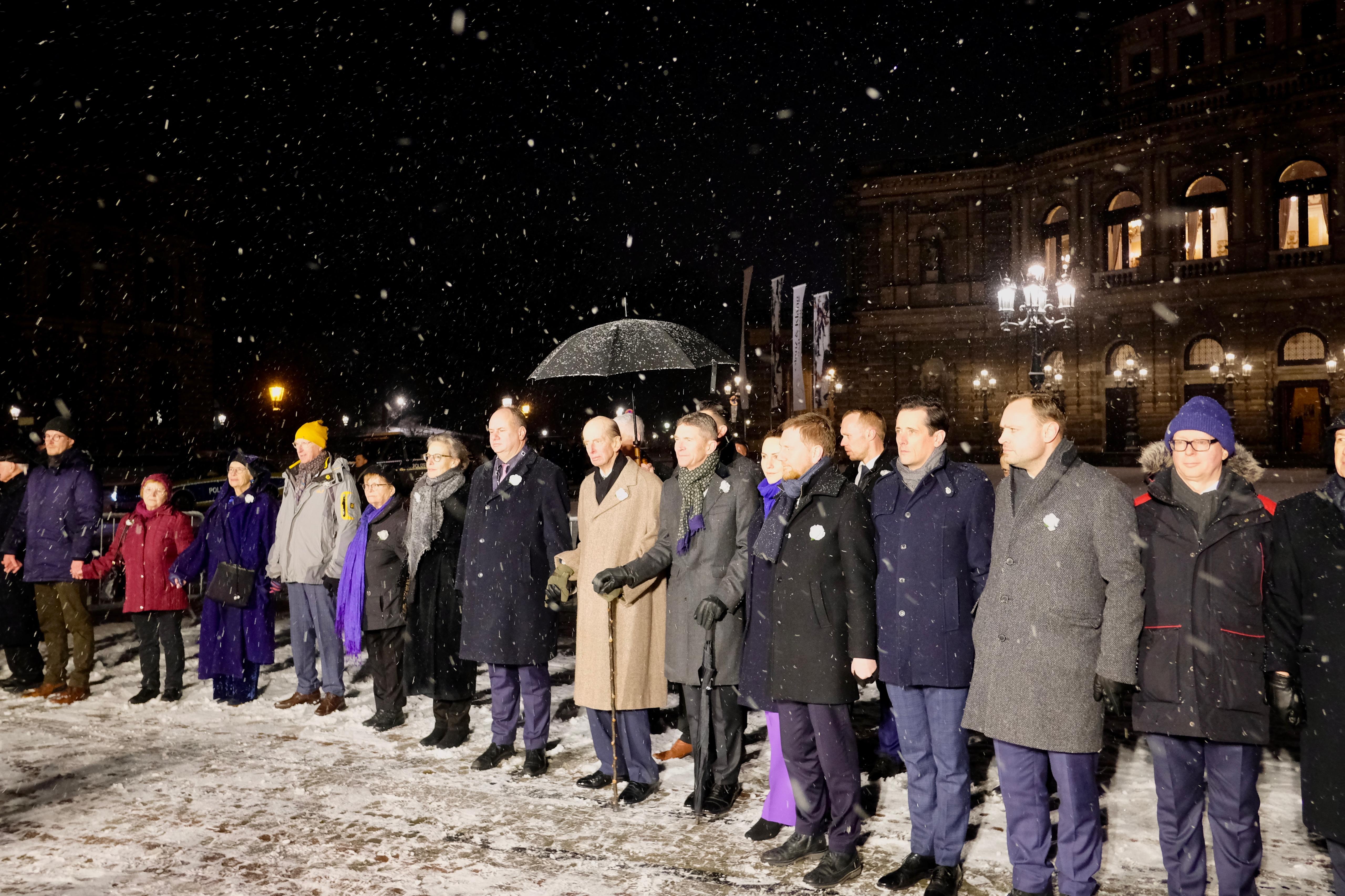 The Duke of Kent stands amid the snowfall and holds hands as part of a human chain by the people of Dresden in remembrance