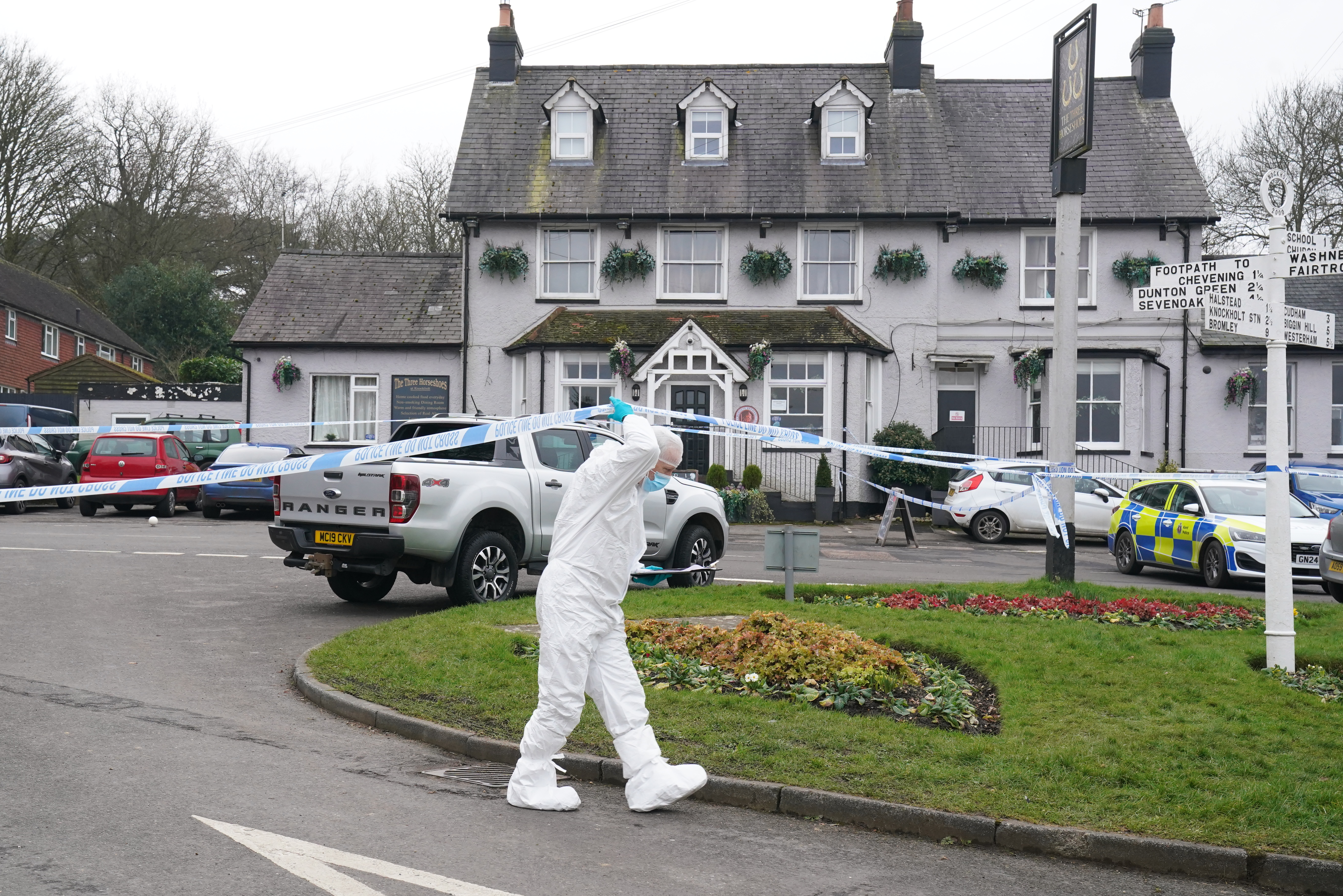 Forensic officer walks under police tape outside a pub