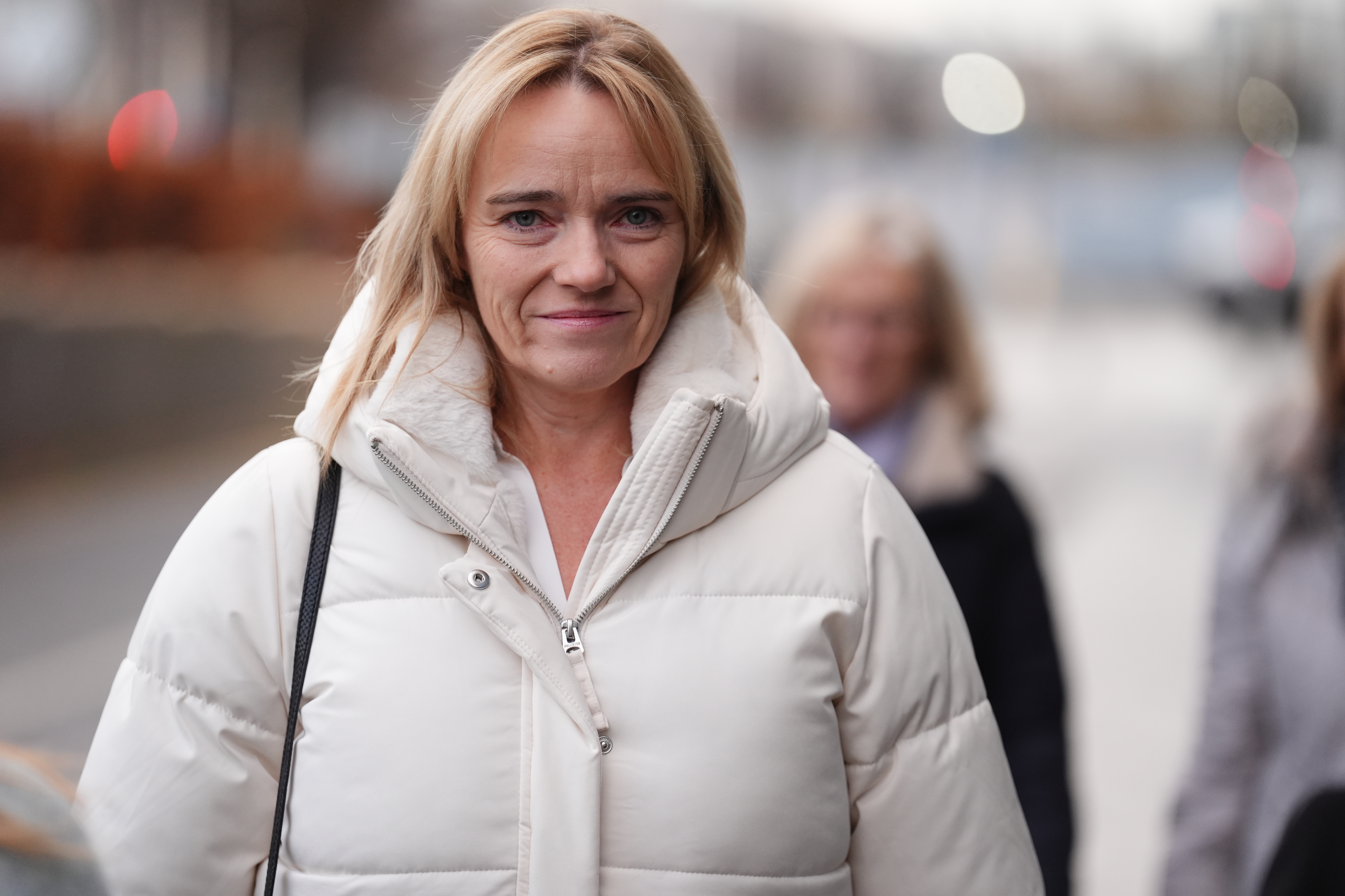 Sandie Peggie smiling while walking outside, wearing a cream puffer coat