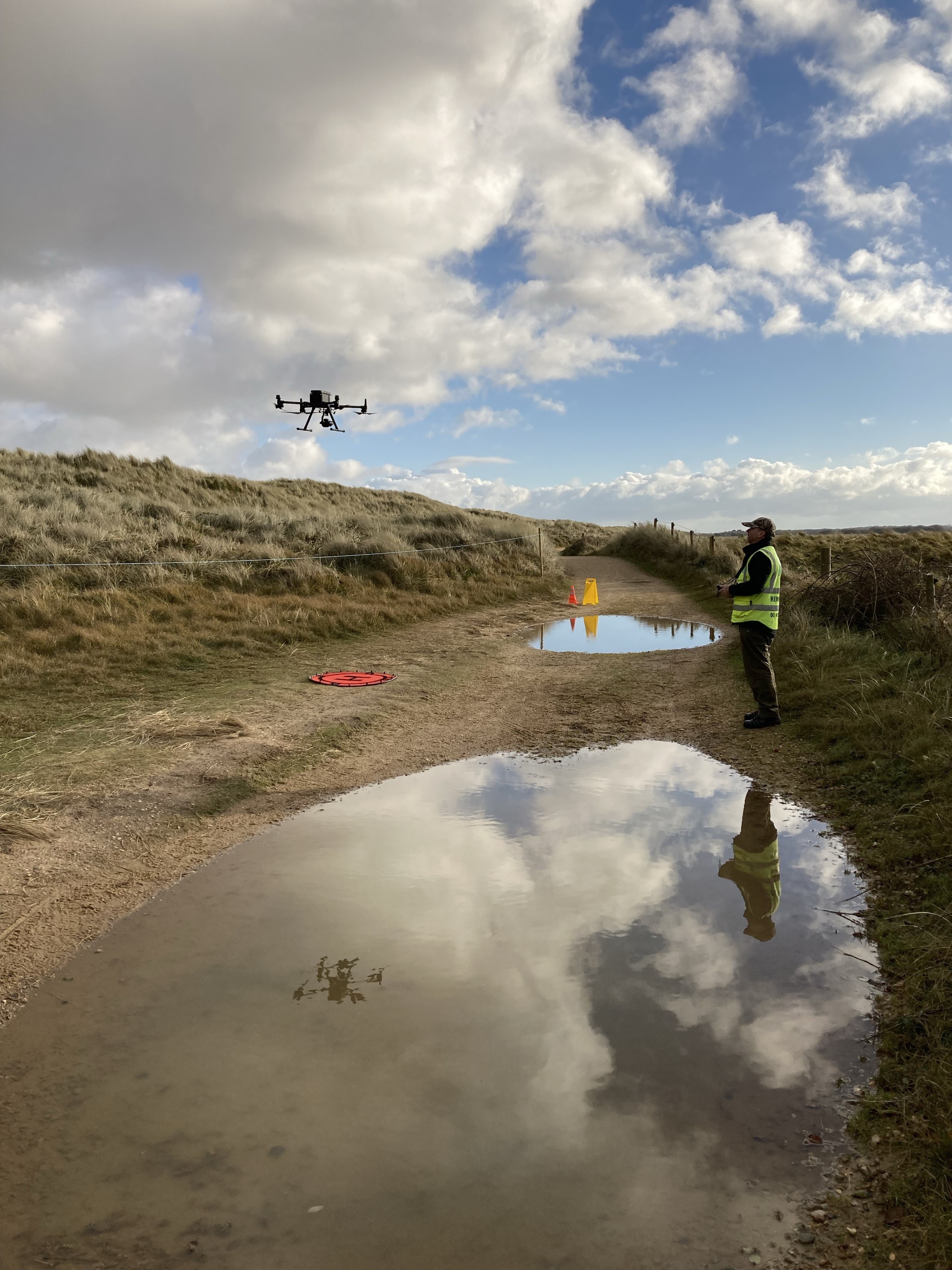 A drone being operated by an officer from Natural England over a beachside path