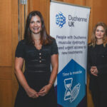 Alex Johnson and Emily Reuben smiling next to a Duchenne UK sign