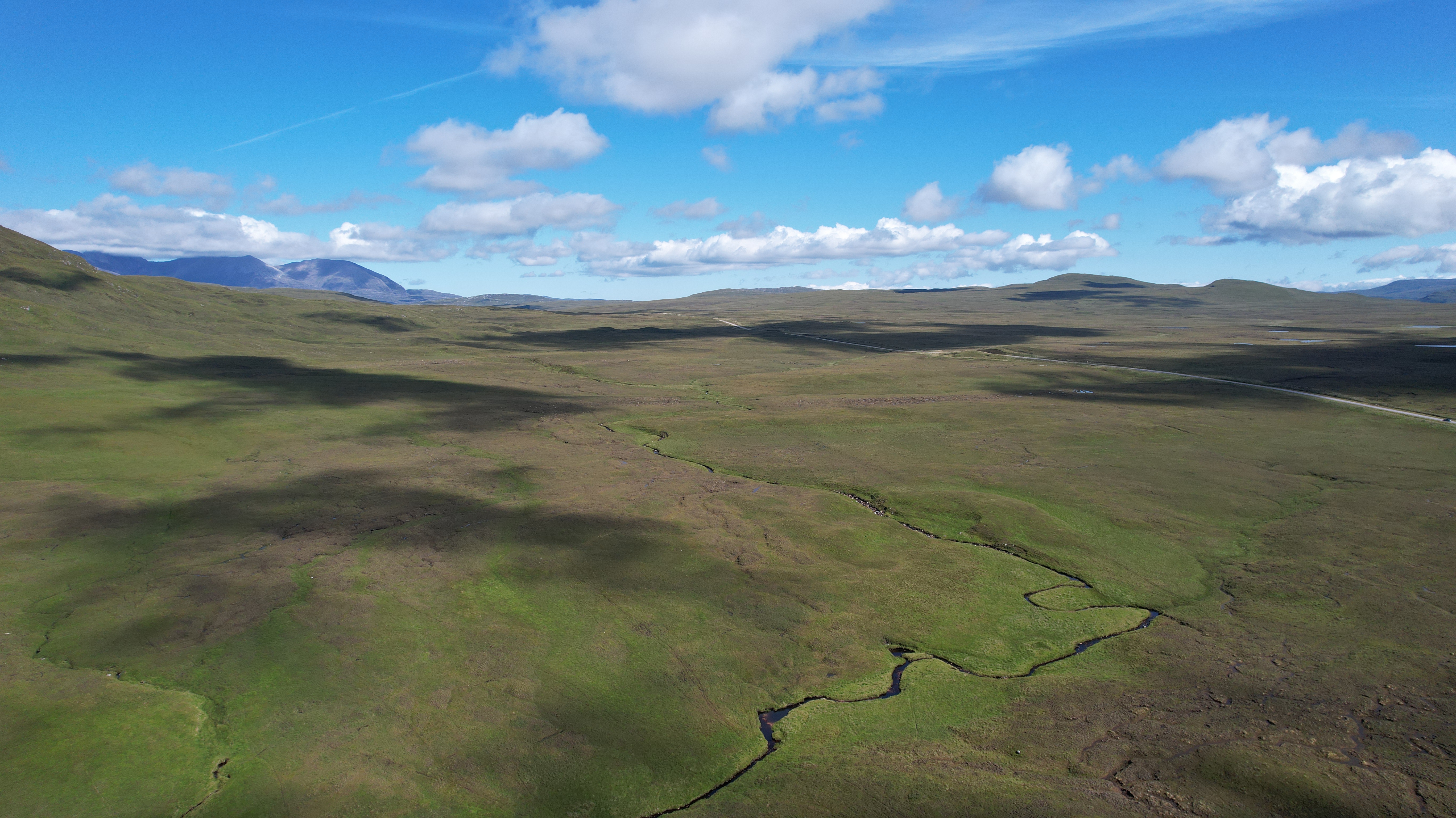 Aerial view of open green space, with mountains beyond, under blue skies