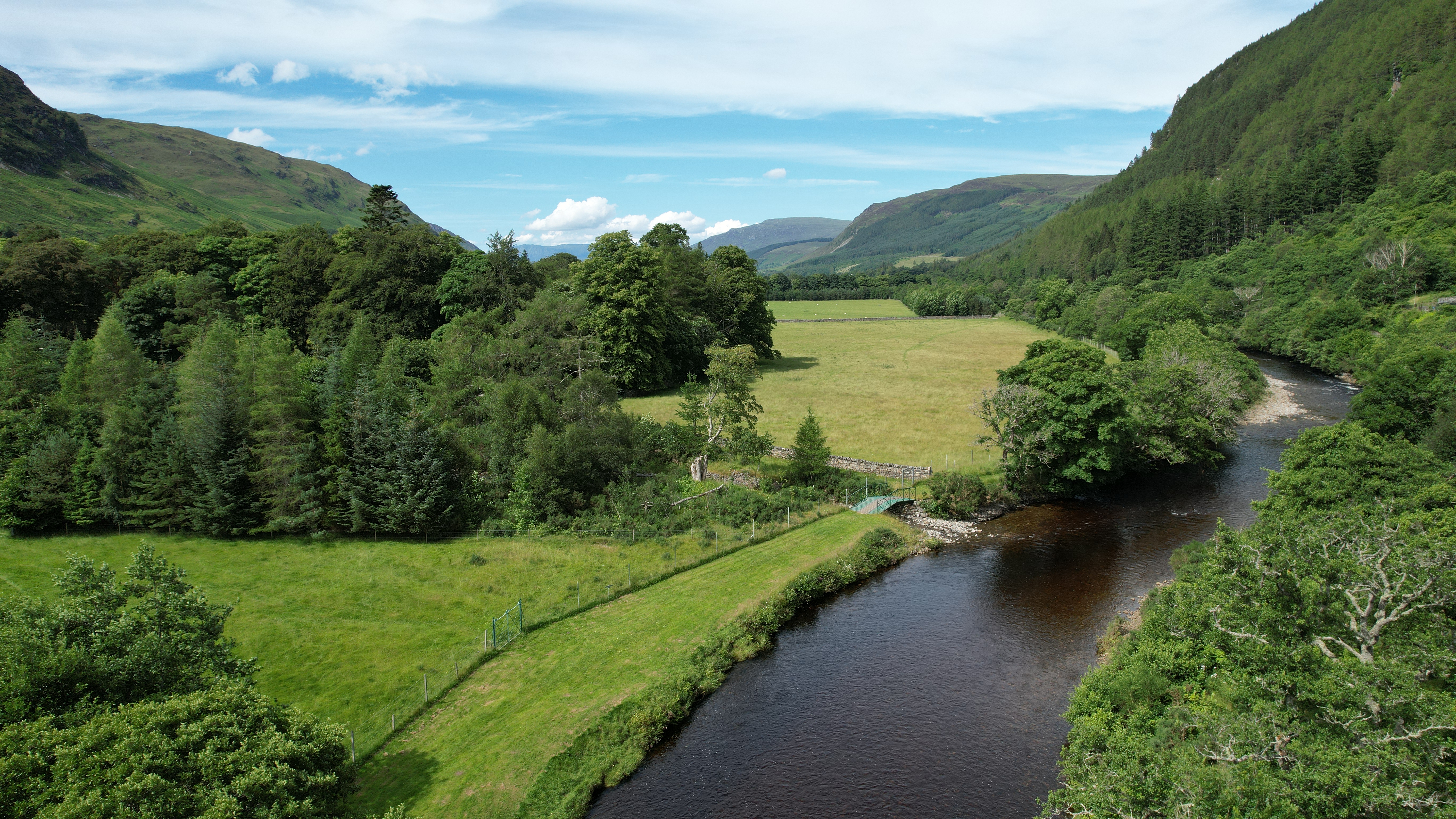 Aerial view of a river, amongst green trees, fields and mountains