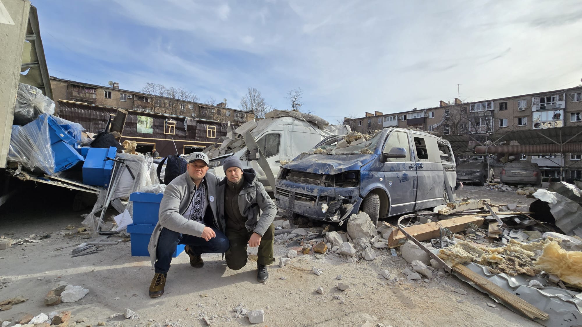 Two men crouching in front of a damaged vans and cars following a missile strike in Ukraine