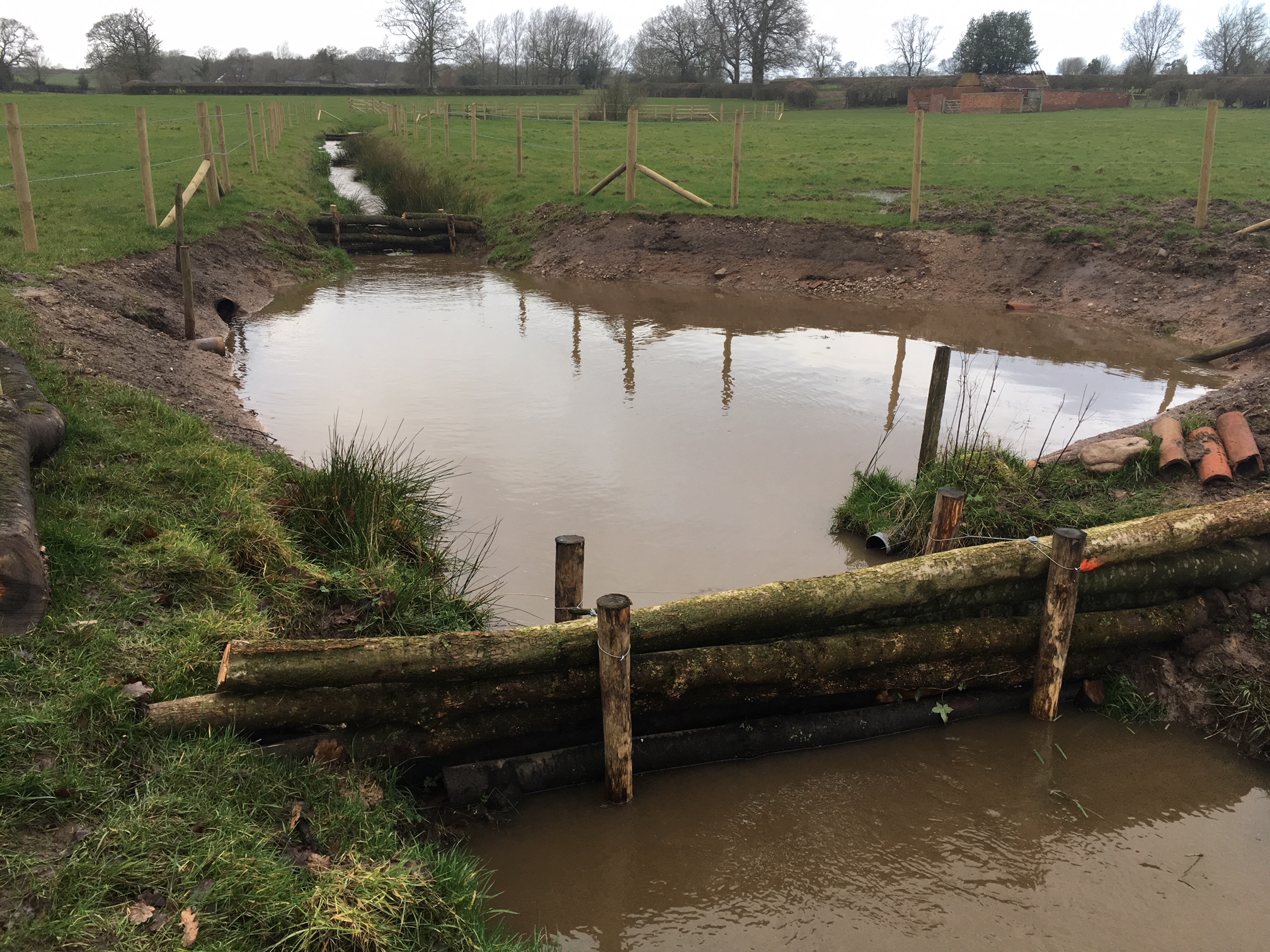 A newly constructed pool with leaky dams made of wooden logs in farmland