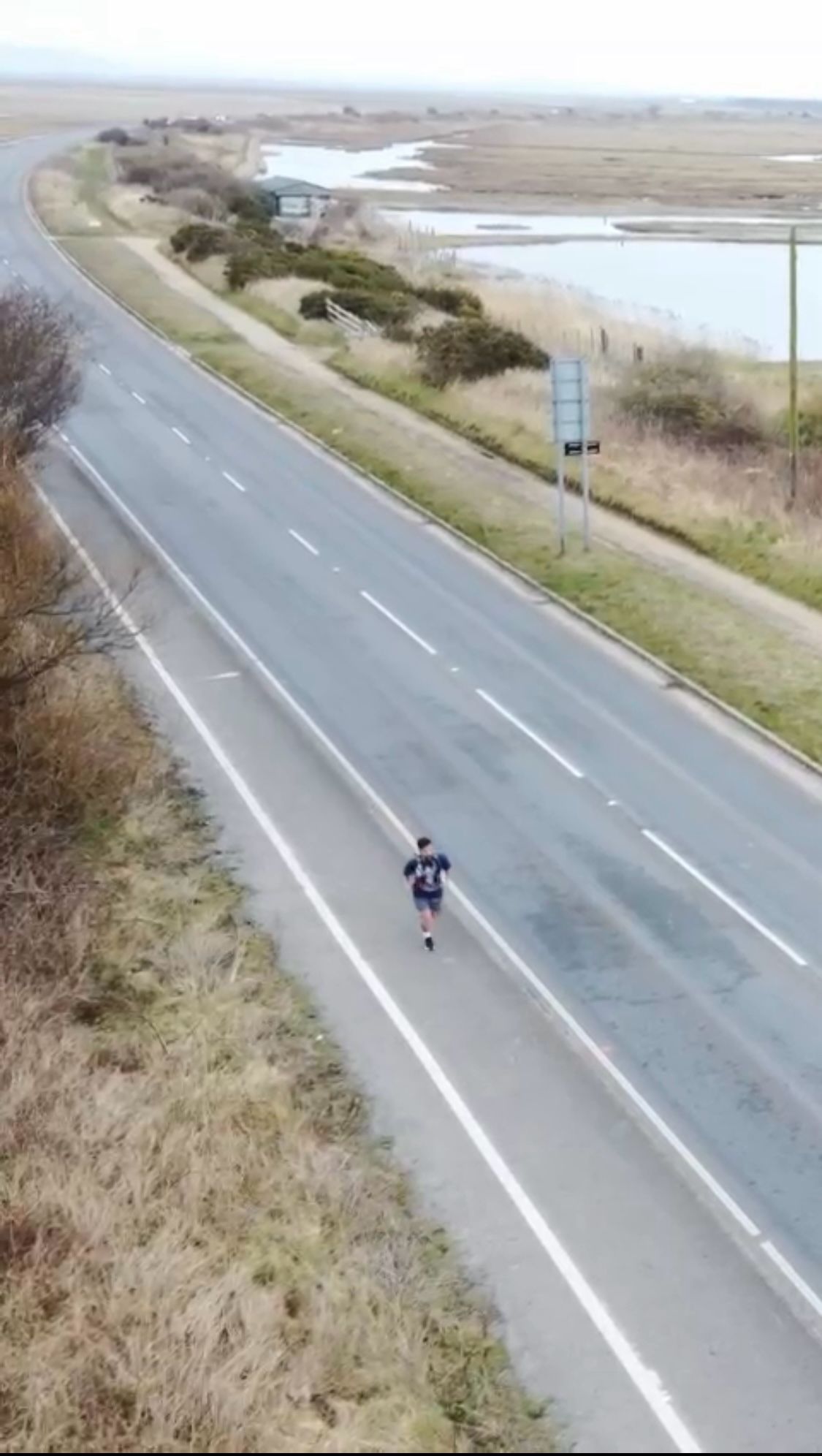 Wide drone shot of a man running alongside a main road in the UK