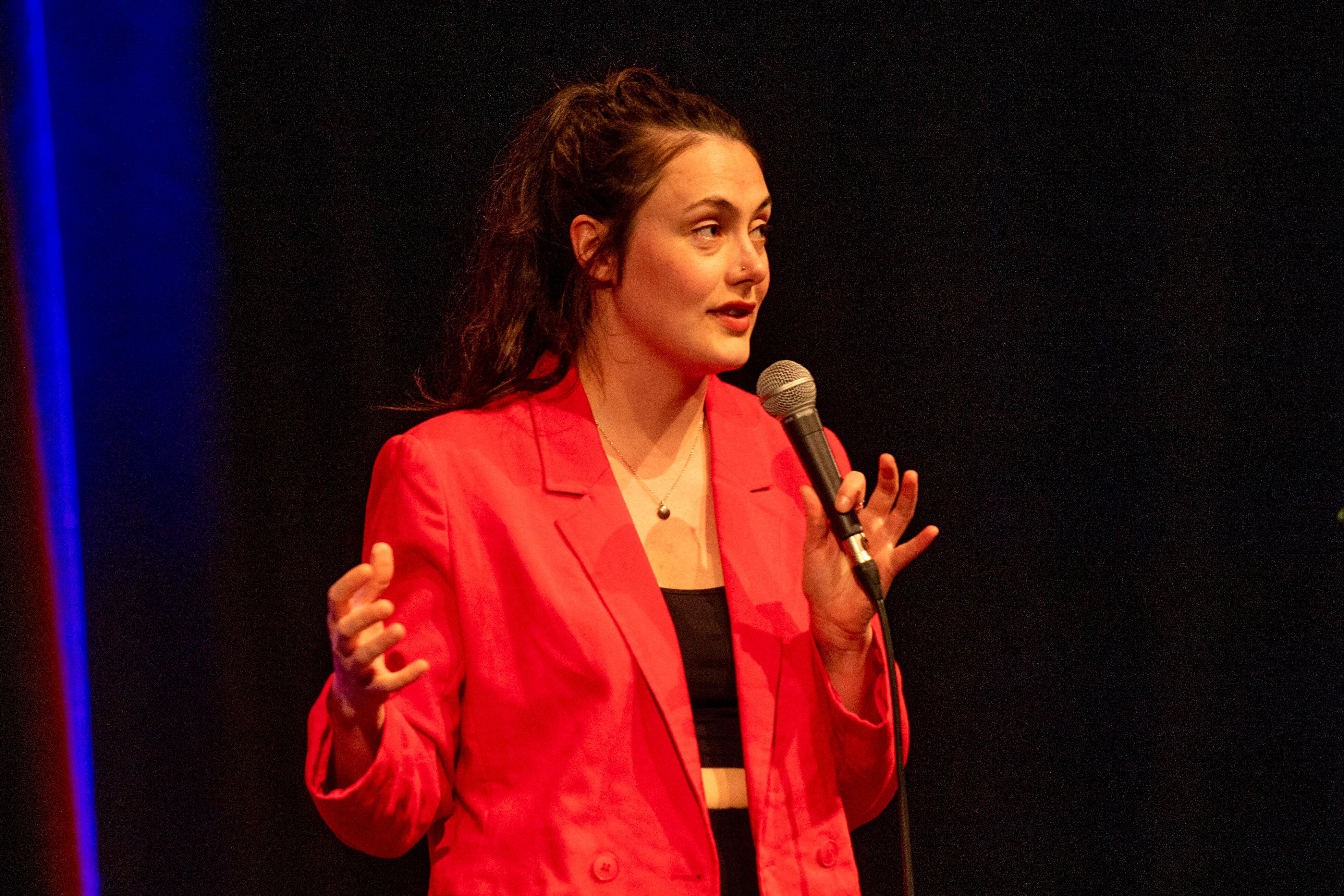 Marjolein Robertson speaking into a microphone she is holding, wearing a red blazer