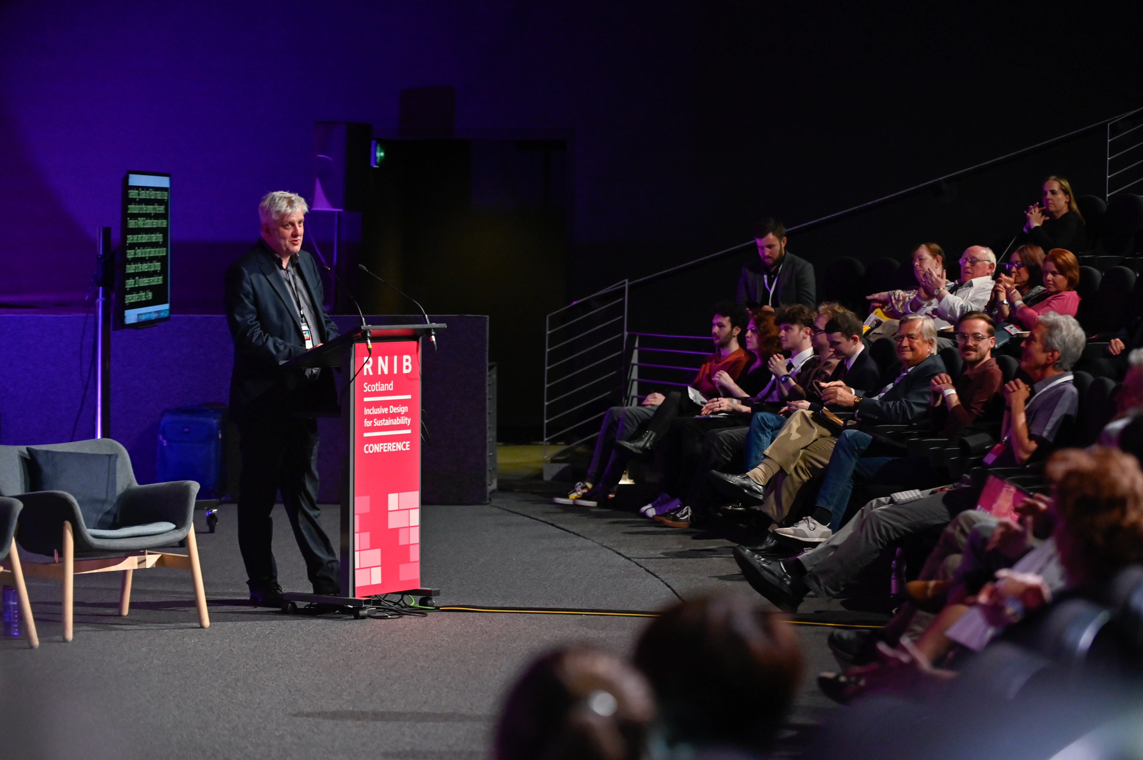 James Adams speaking to an audience from a lectern with RNIB Scotland on it