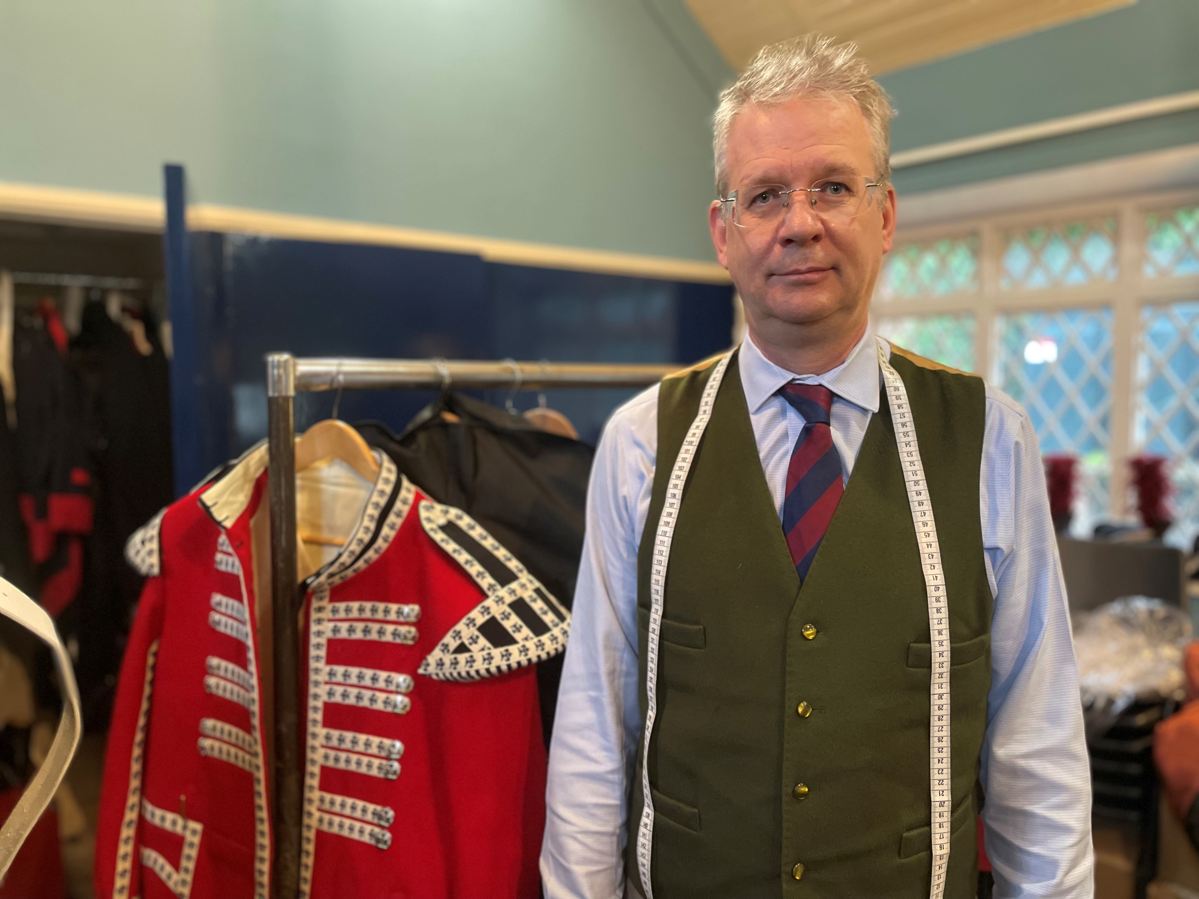 Lee Dawson, with measuring tape round his neck, standing in front of a rack of uniforms