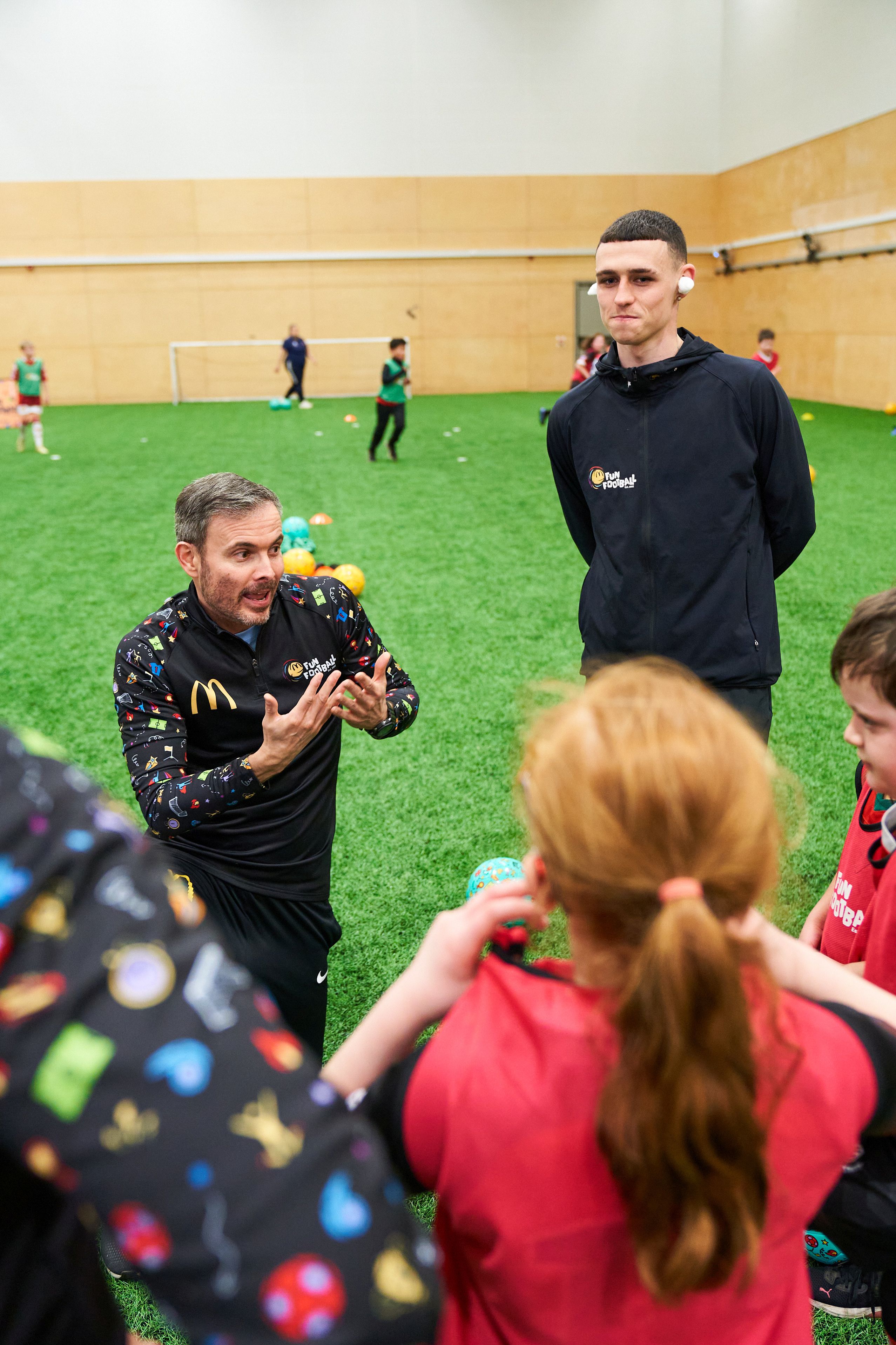 Manchester City's Phil Foden wears cotton wool in his ears as a coach uses sign language to speak to children with hearing impairments