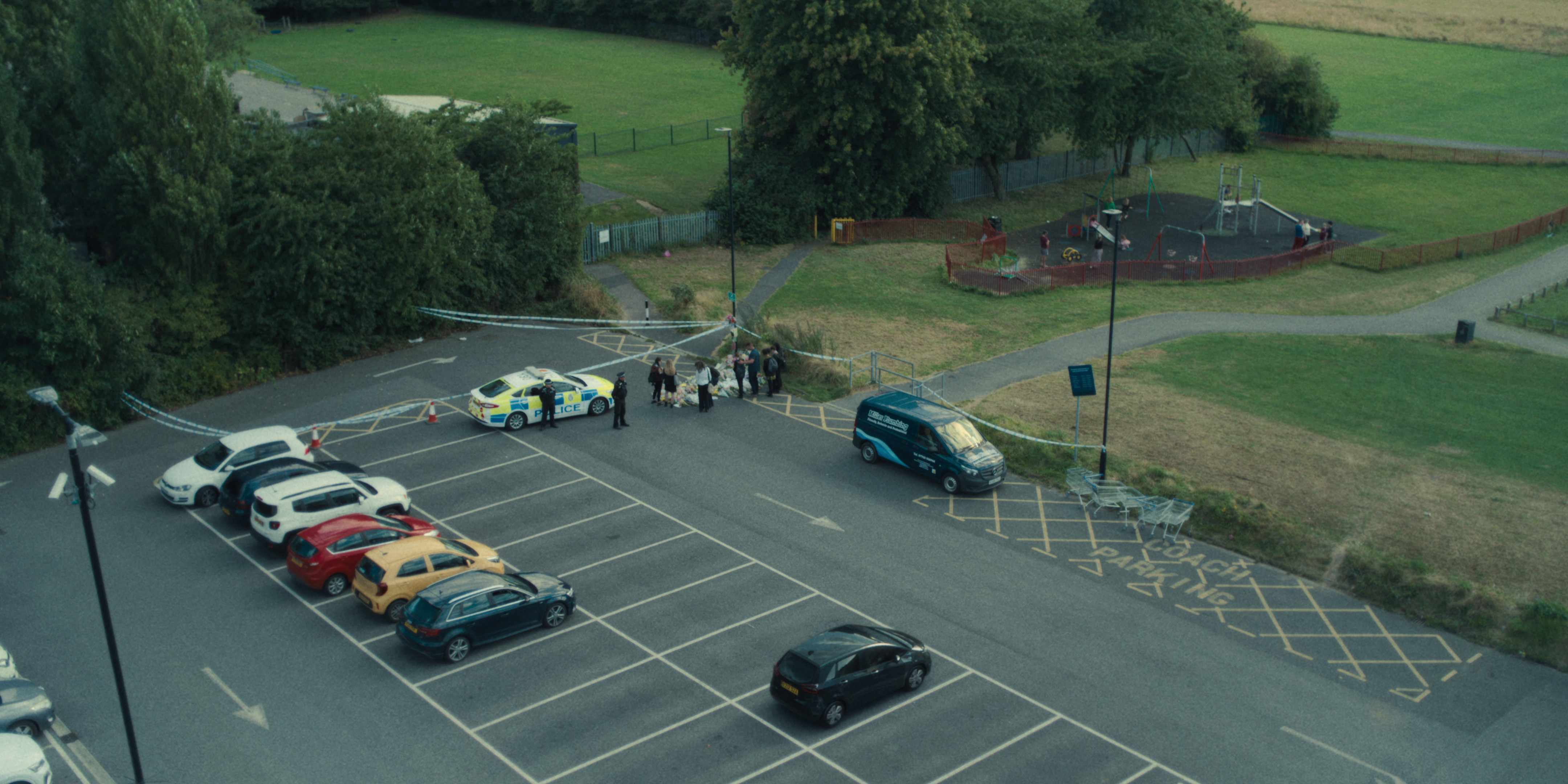 A scene from Adolescence showing floral tributes in a car park from above