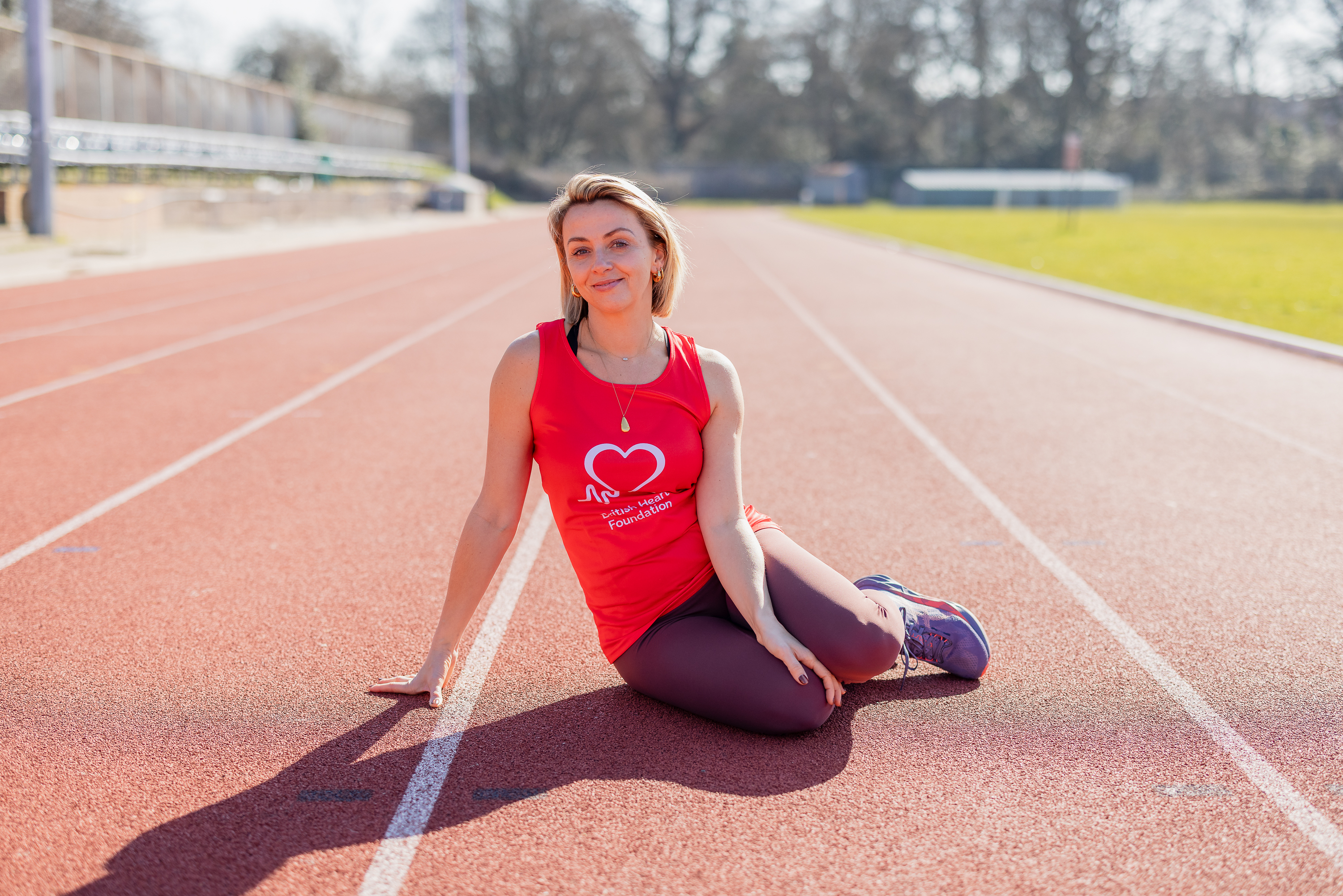 Actress Lisa McGrillis sitting on a running track wearing a red British Heart Foundation vest 