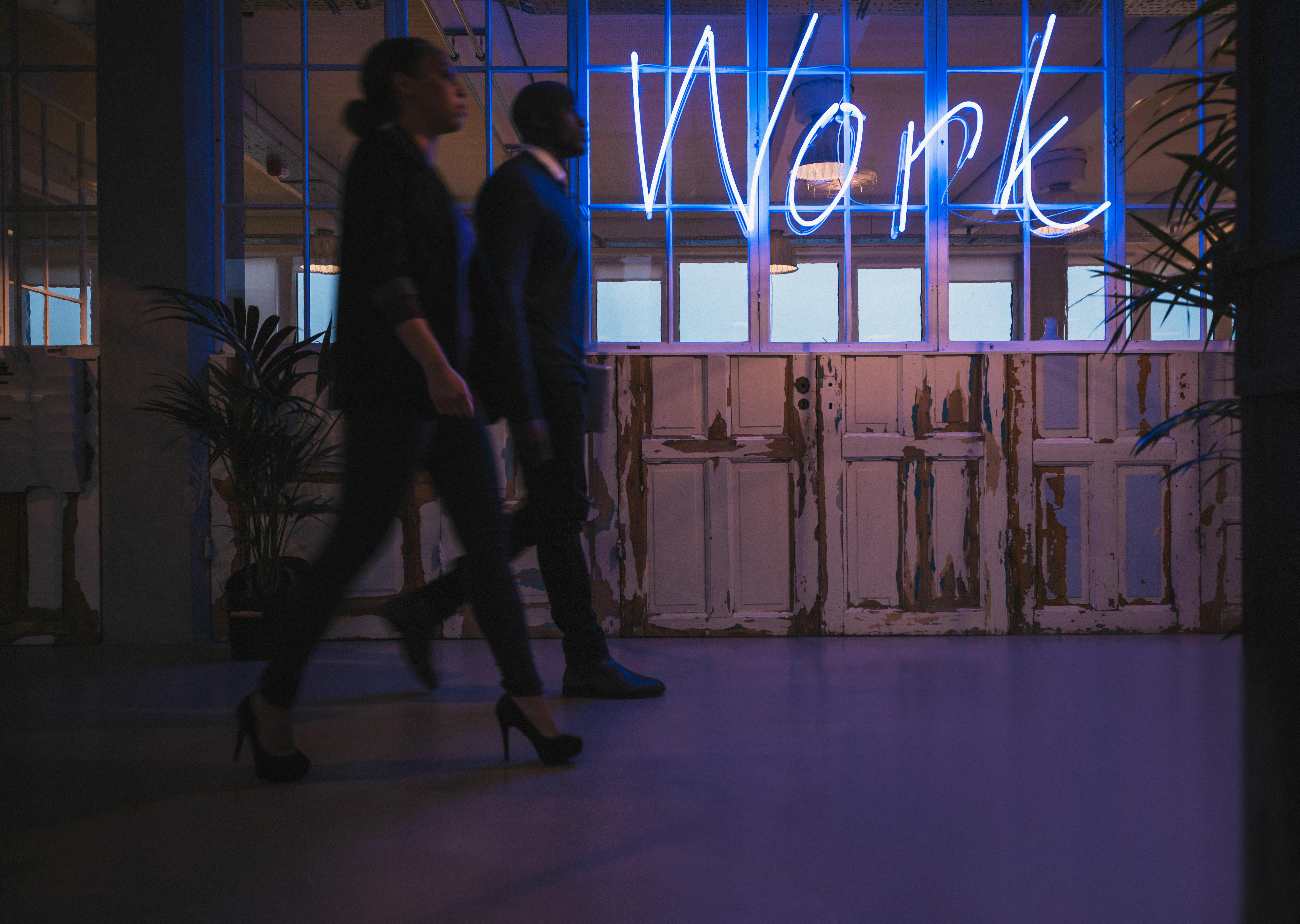 Young business people walking through an office corridor with a neon light work sign