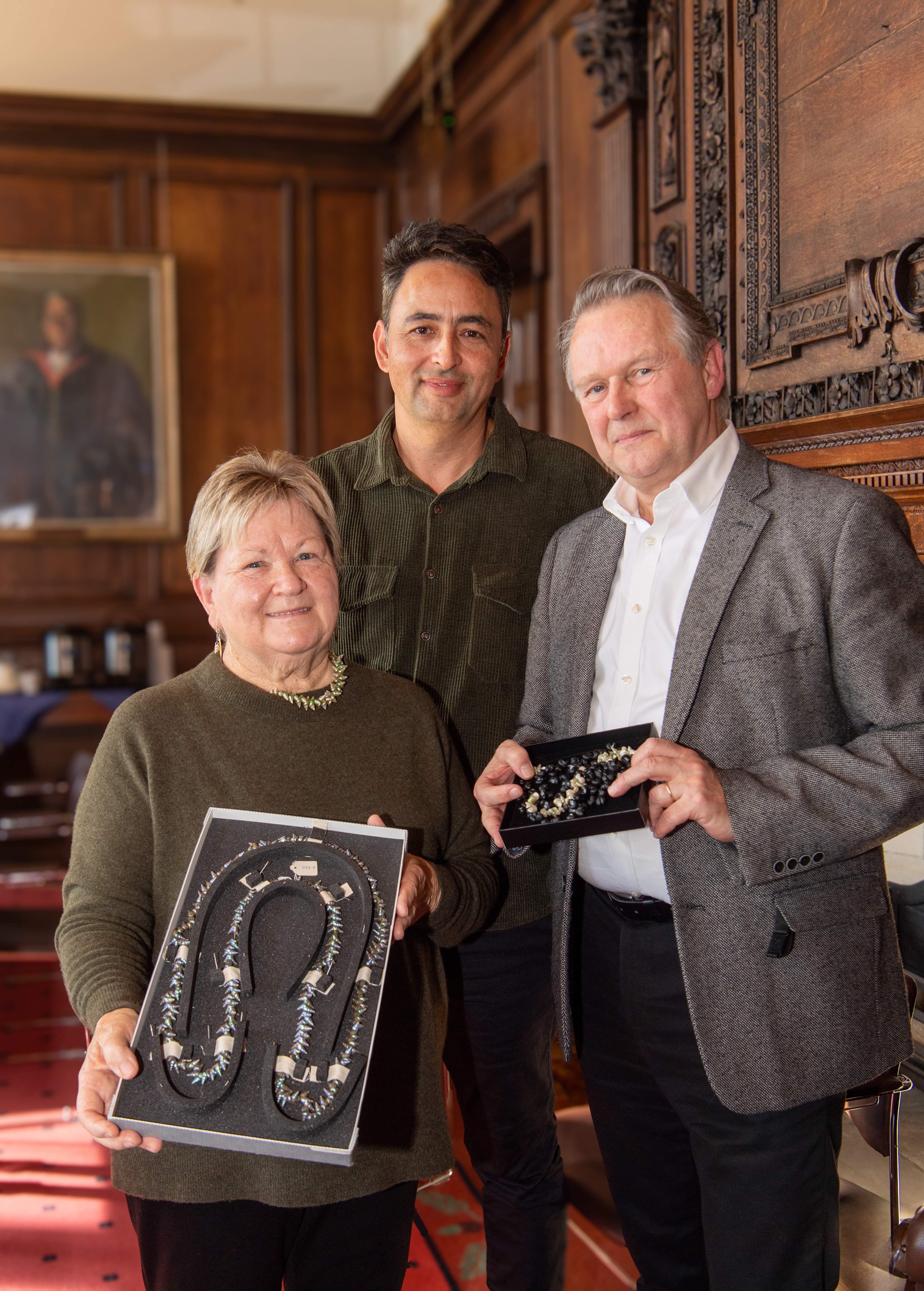 Three people standing in a row, one holding a necklace in a box