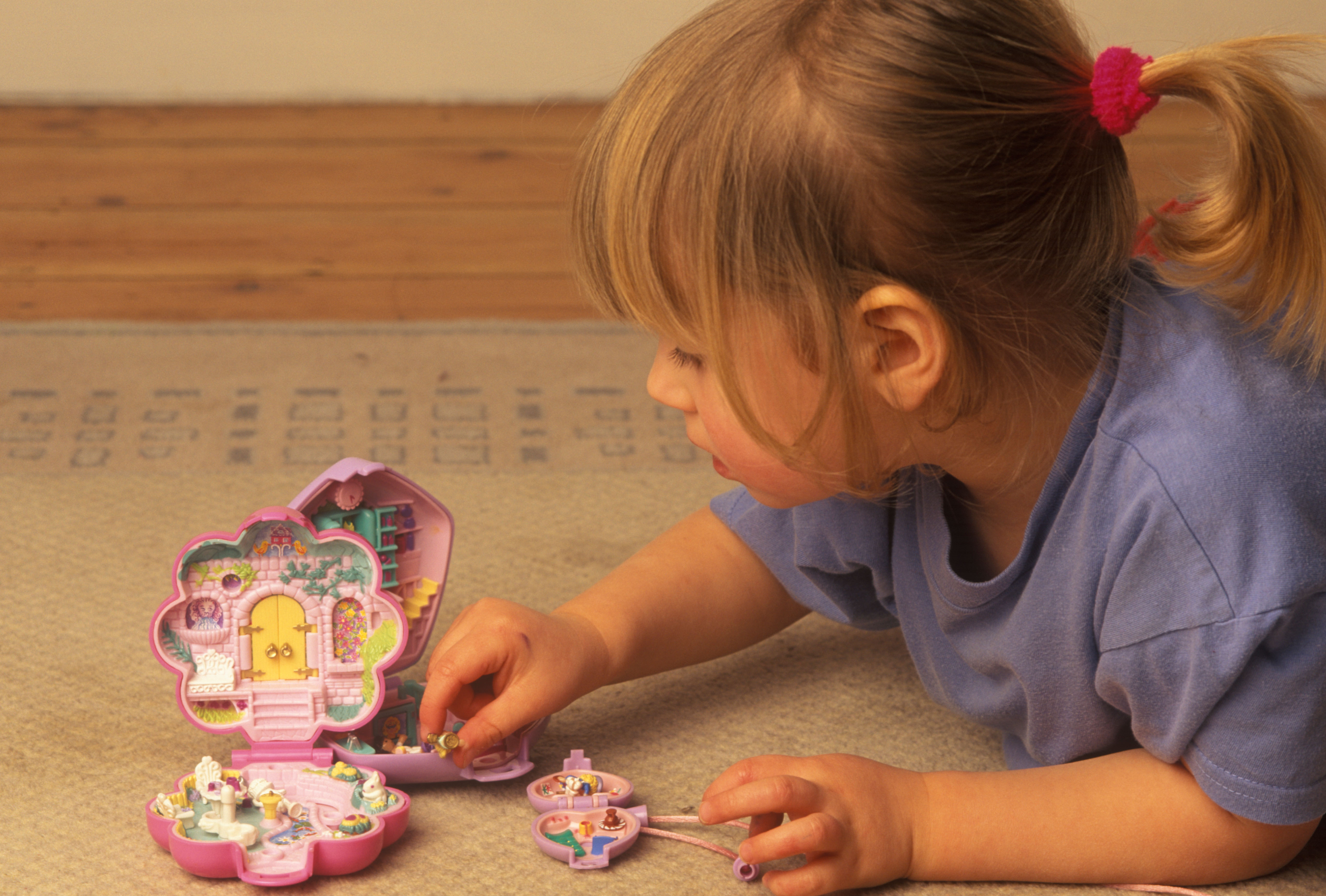 A little girl lying on the floor playing with Polly Pocket toys