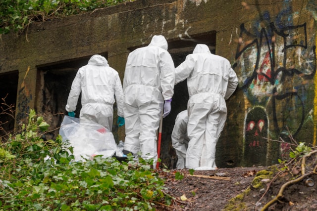 Police in white boiler-suits searching a bunker