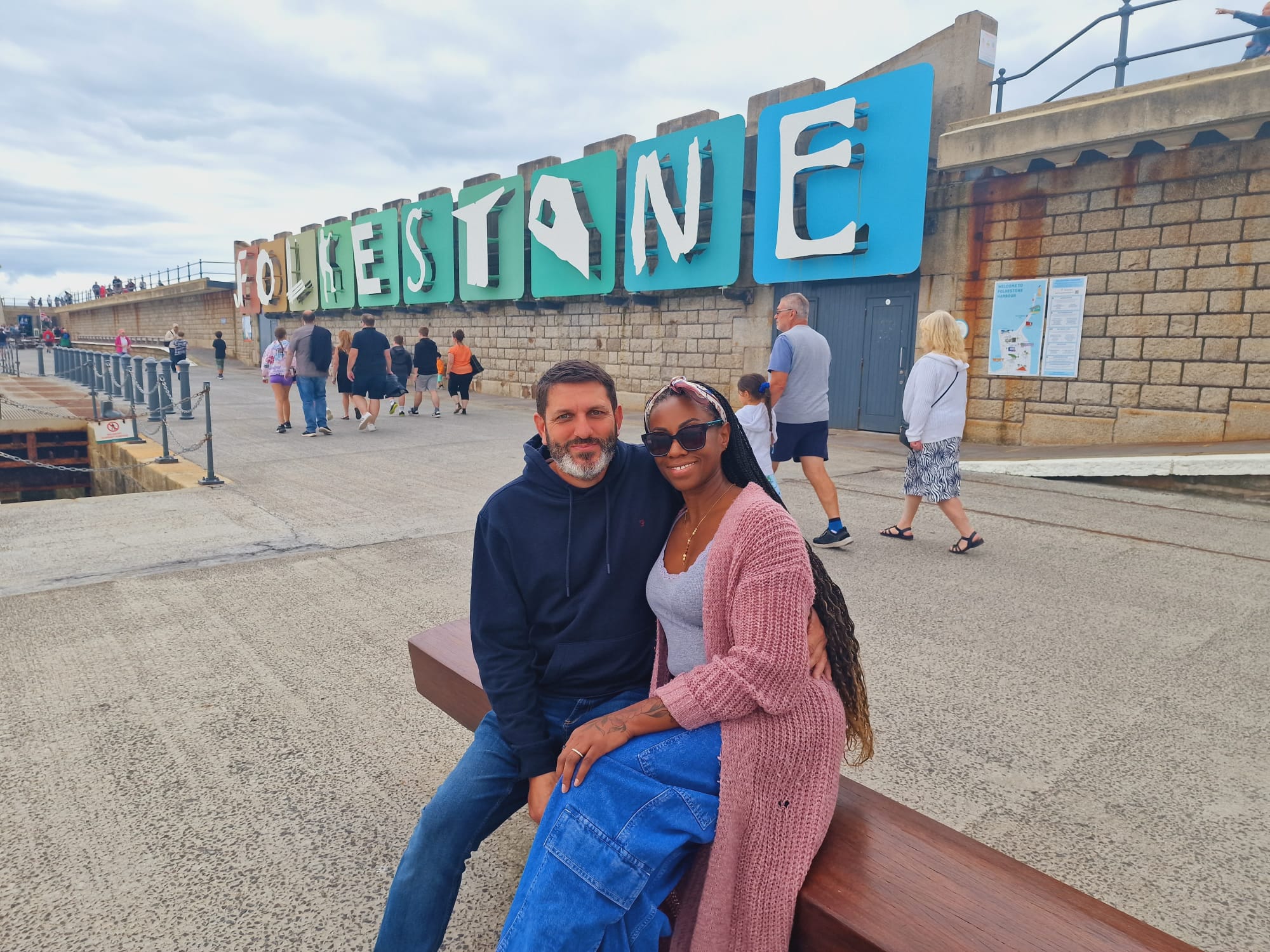 Couple sat on a bench in front of a Folkestone sign